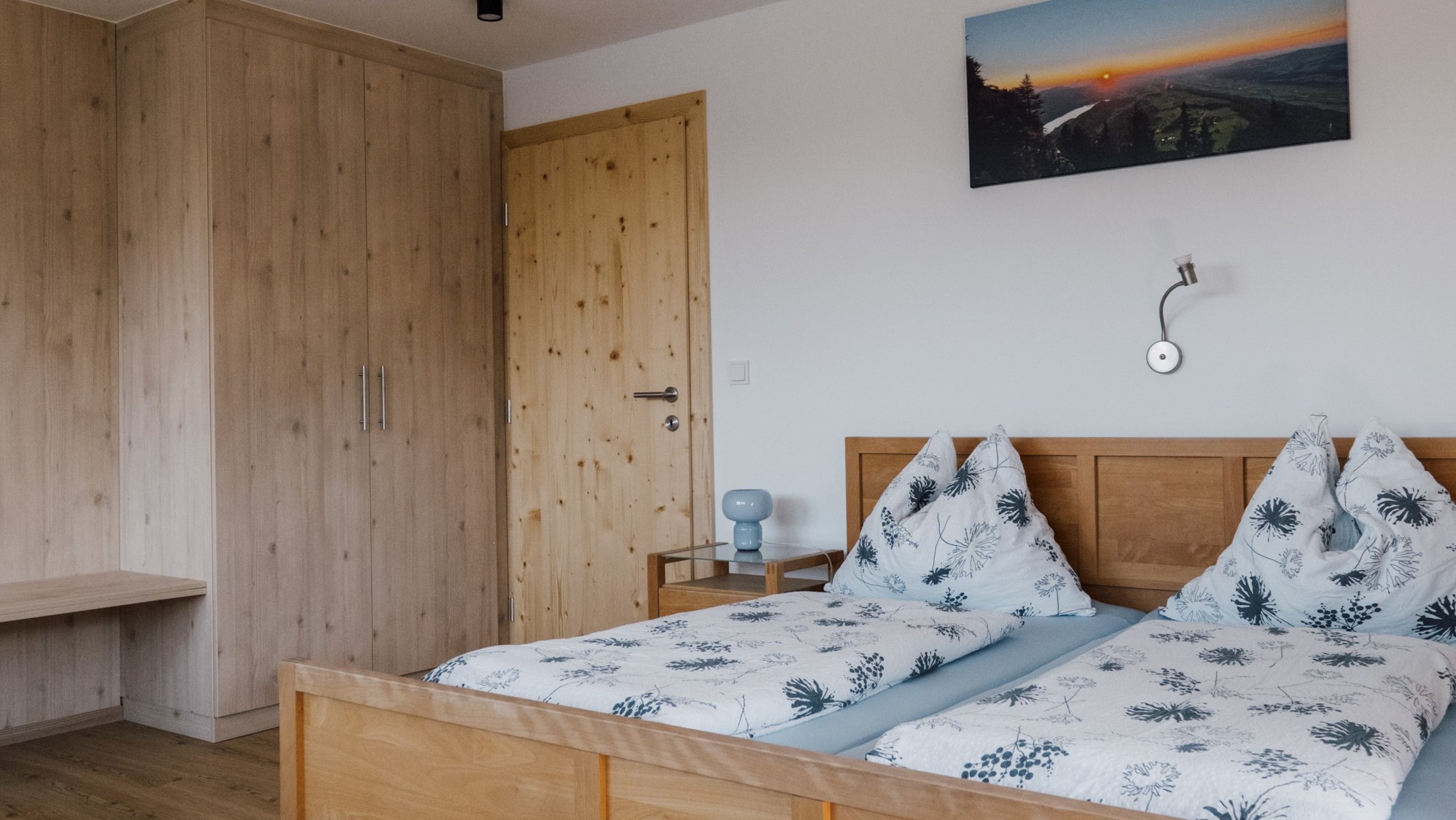 Helles Schlafzimmer mit Holzbett, gemusterten Bettwaren und minimalistischer Dekoration.