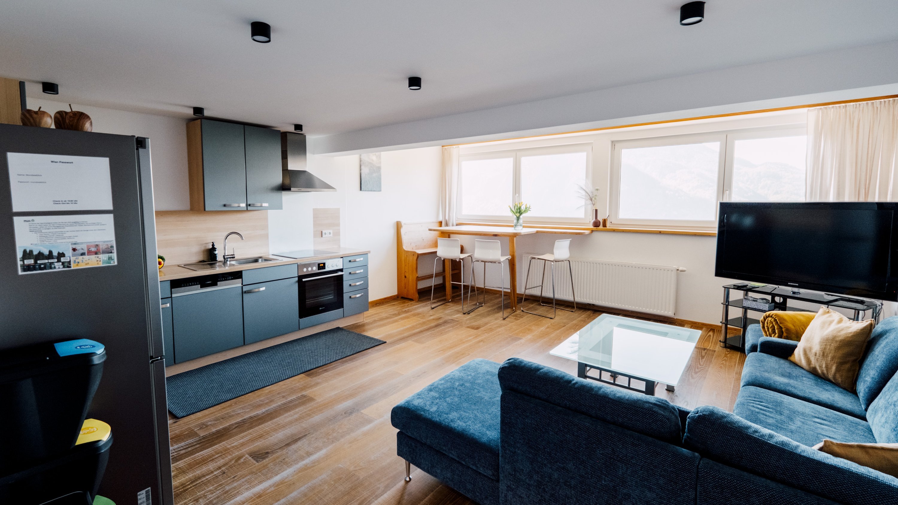 Innenansicht einer modernen Wohnung mit Küche und Wohnbereich, große Fenster und stilvolle Möbel.