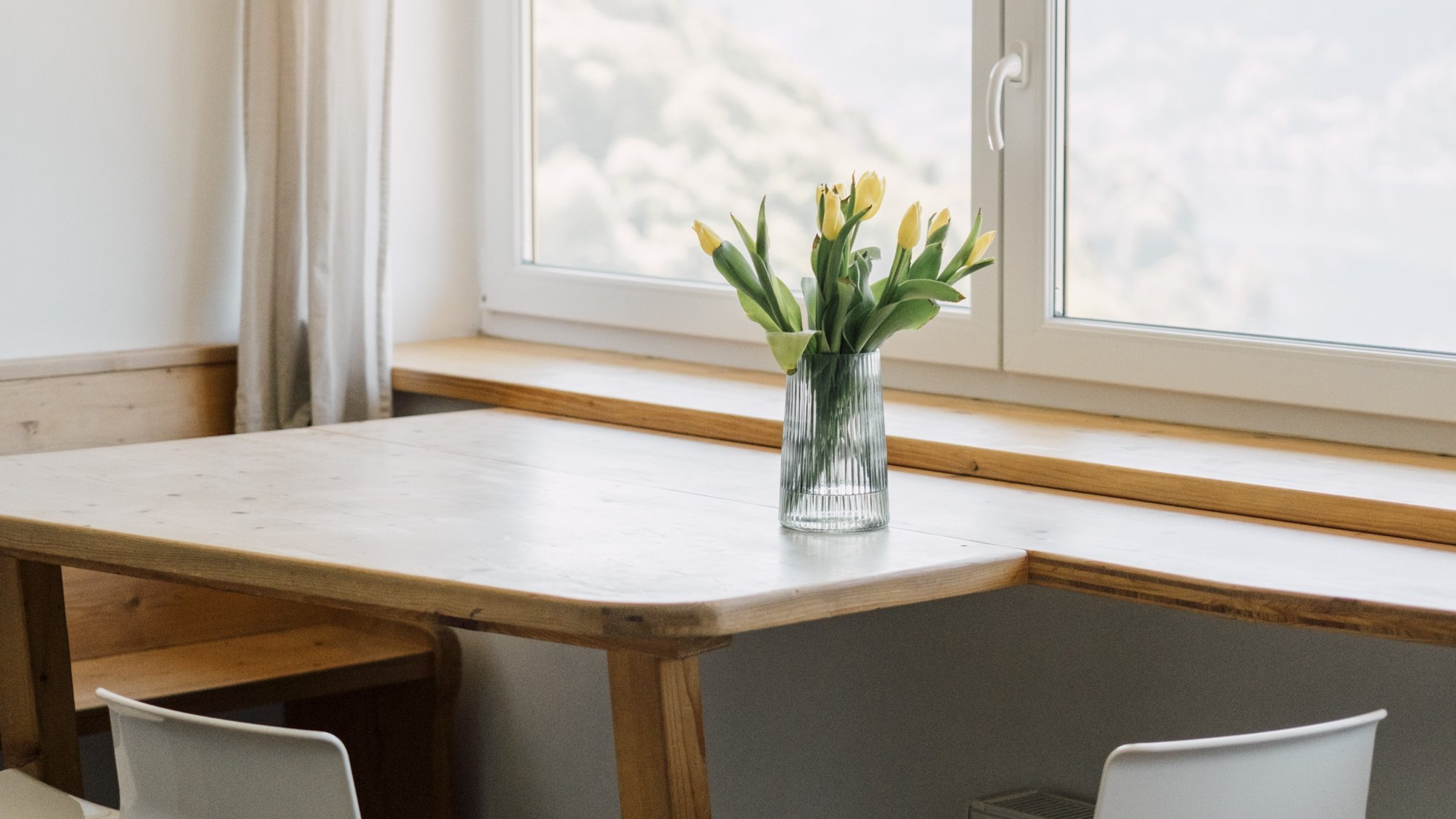 Heller Essbereich mit Holztisch, weißen Stühlen und einer Vase mit Tulpen auf dem Tisch