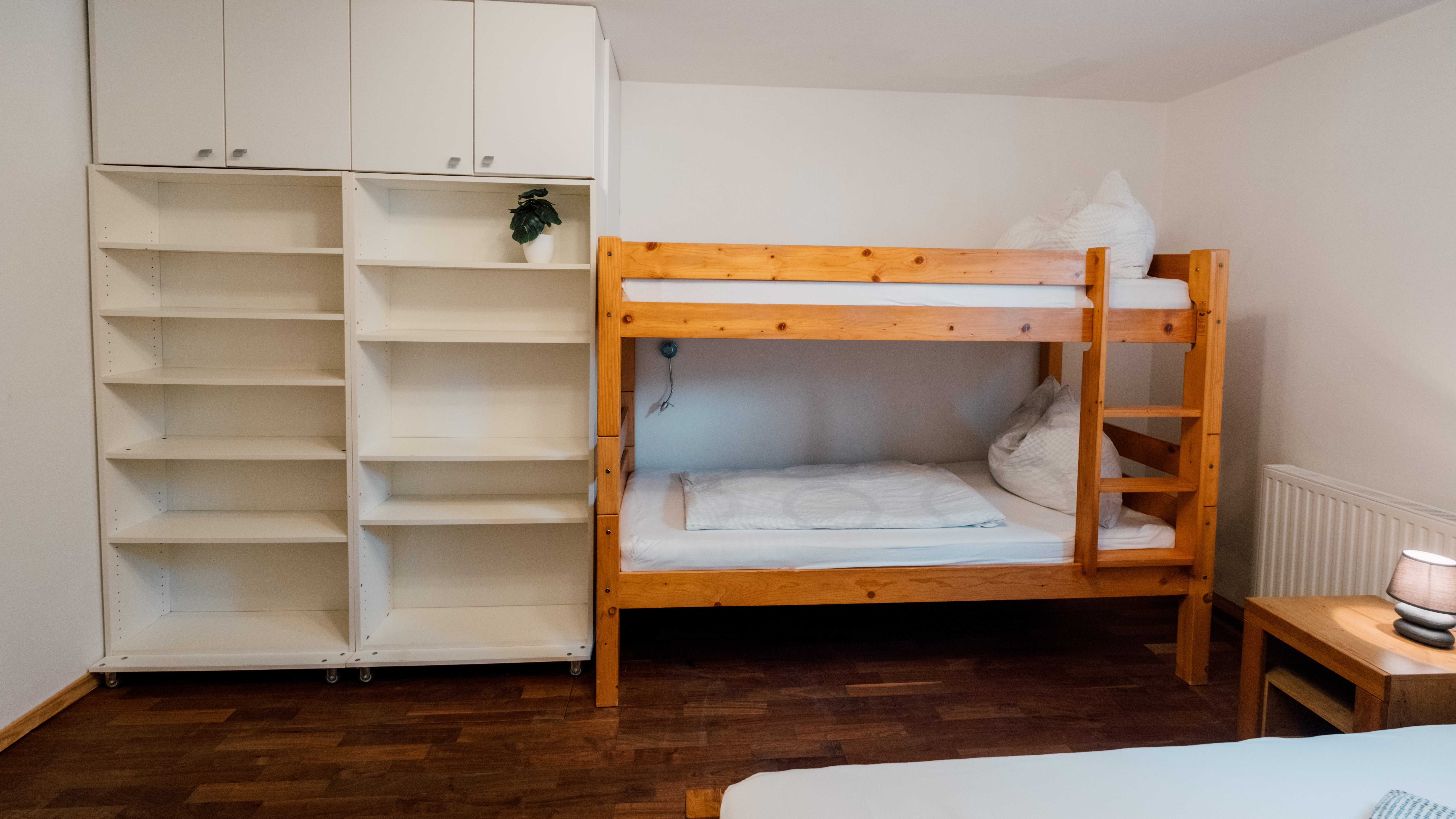 Ein einfaches Schlafzimmer mit einem Holzstockbett und einer weißen Regaleinheit.