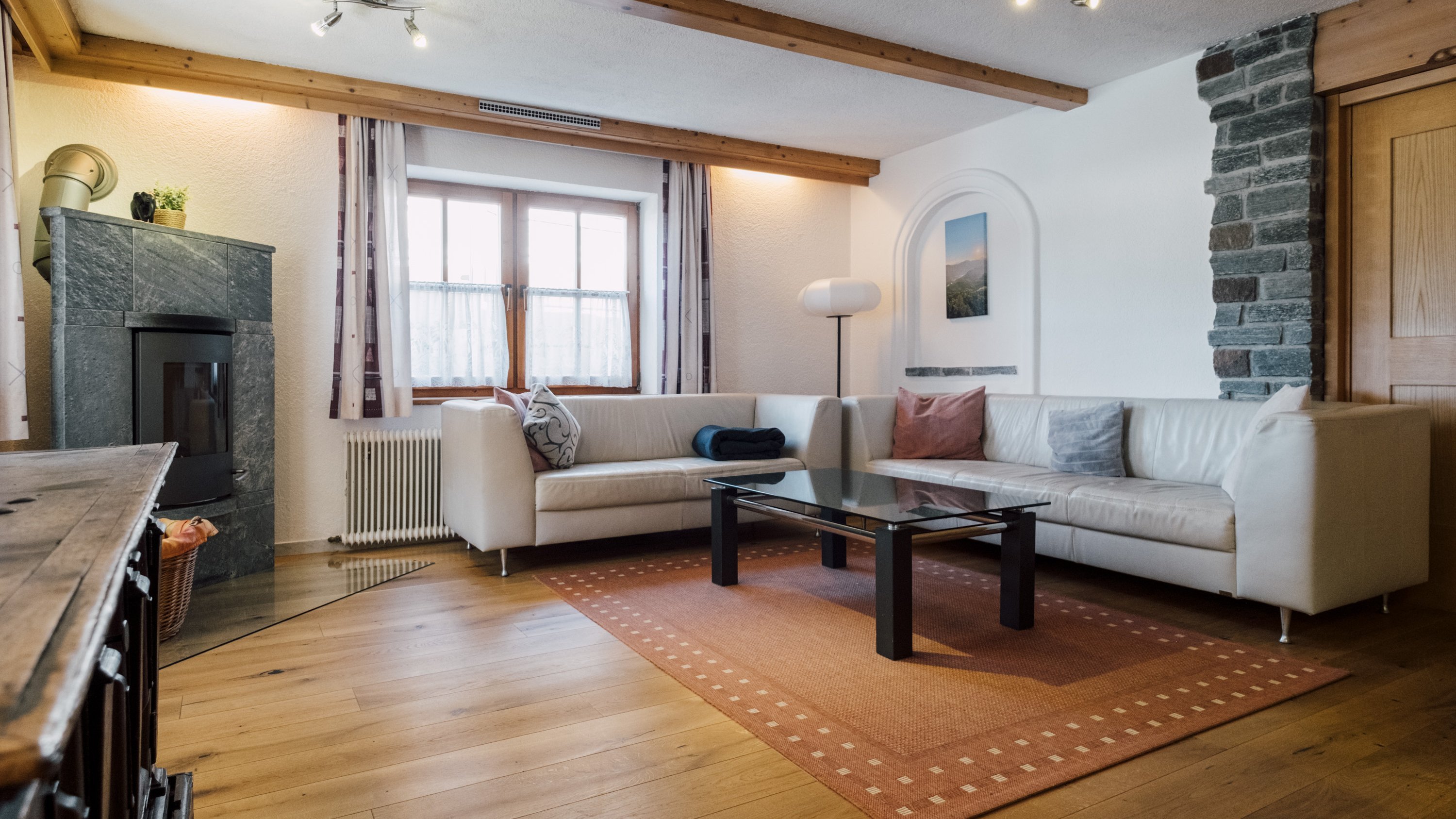 Ein modernes Wohnzimmer mit einem weißen Sofa, Glastisch und einem Kamin unter einem großen Fenster.