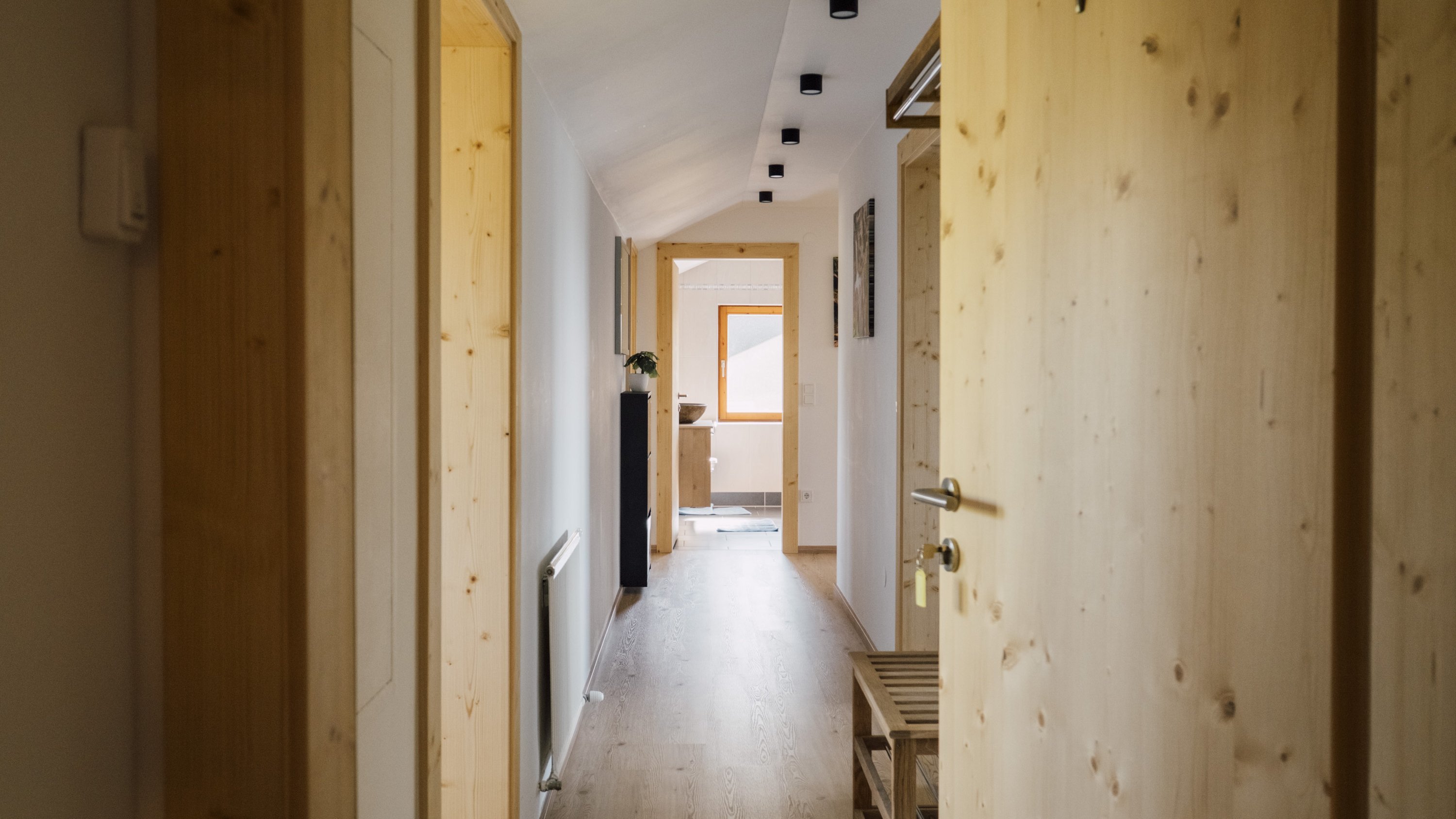 Flur mit Holzvertäfelungen und modernen Türen, hellem Holzboden und indirekter Deckenbeleuchtung