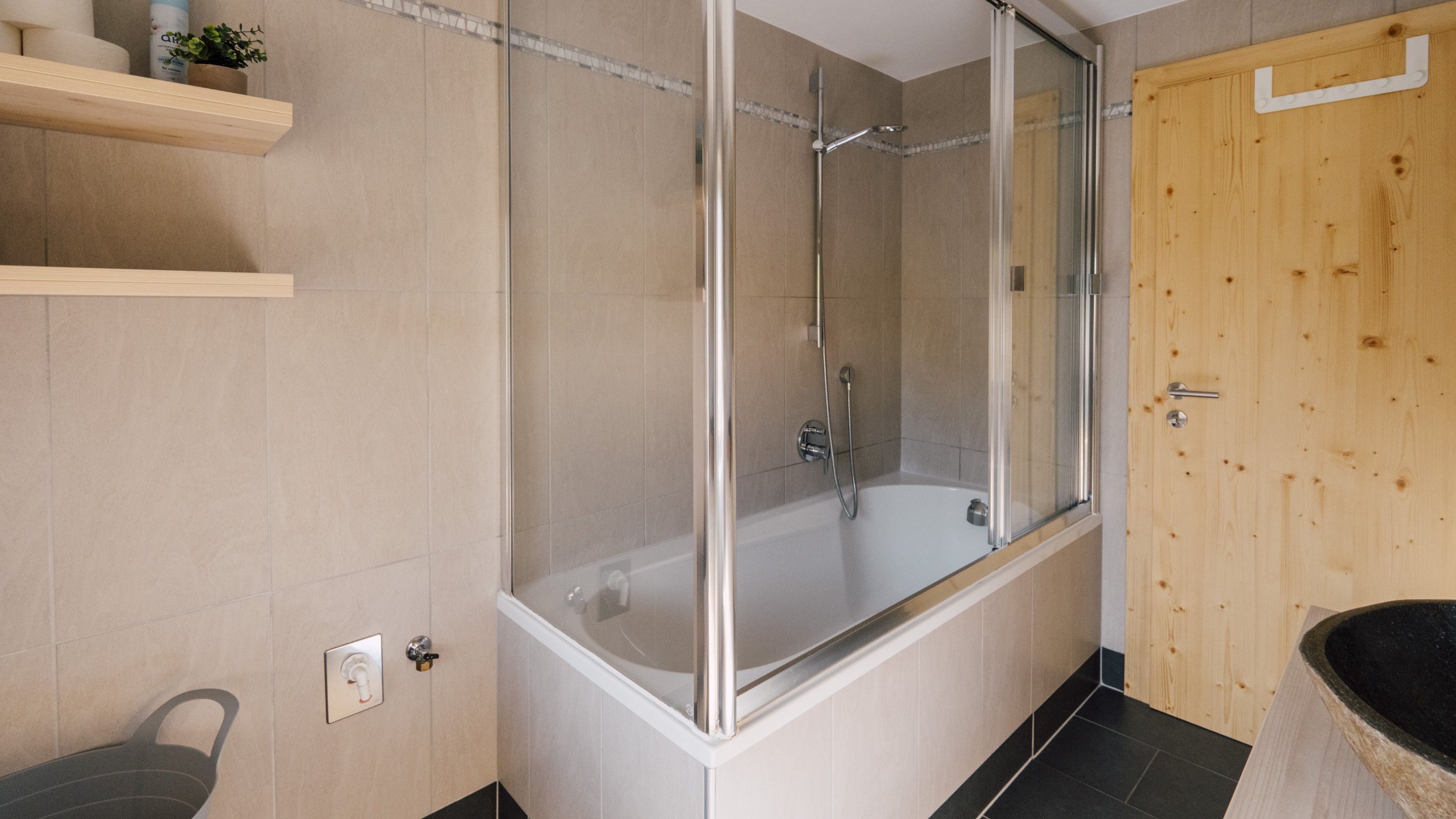 Badezimmer mit Badewanne und Duschabtrennung aus Glas sowie Holzdetails und neutralen Fliesen