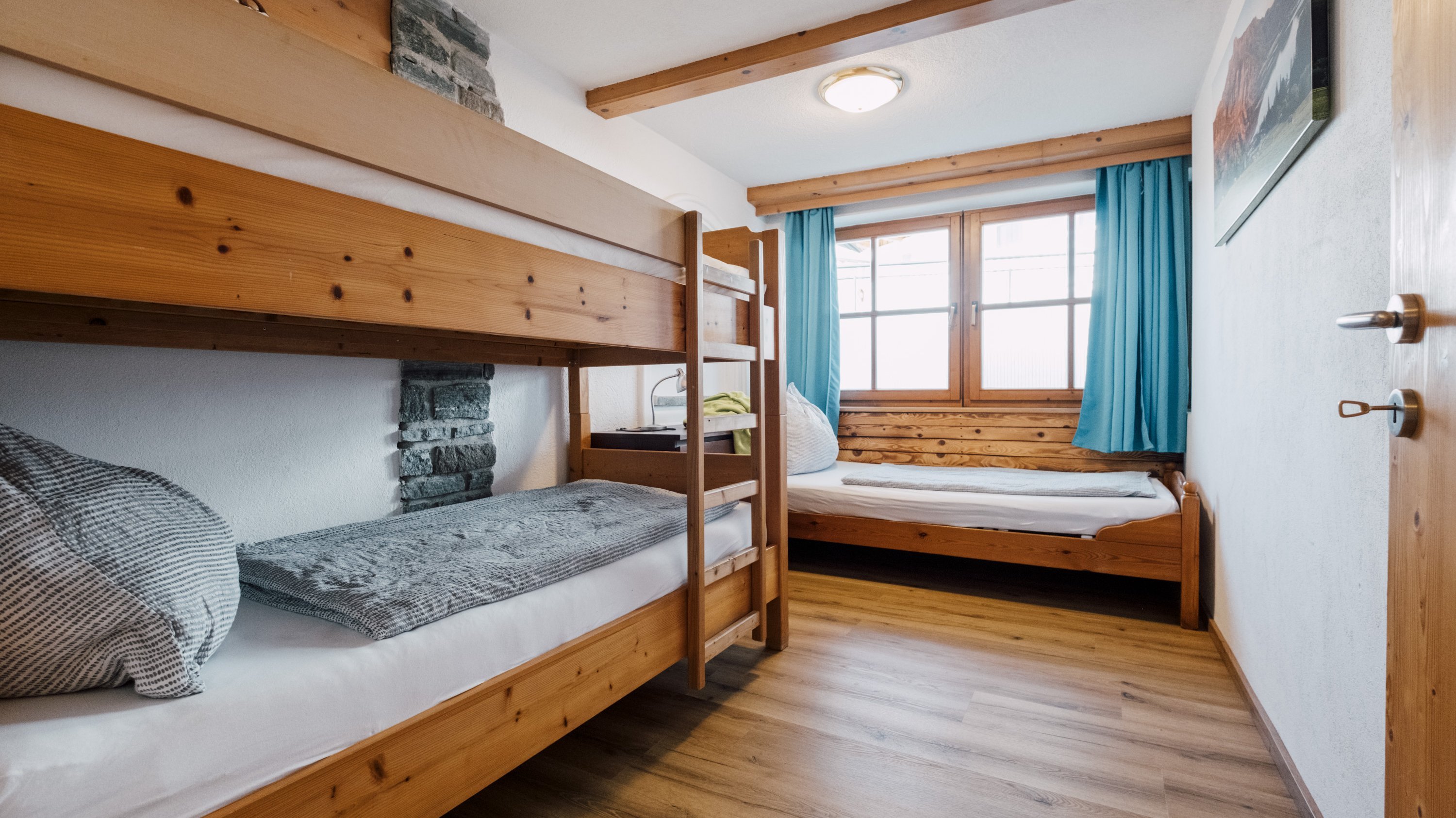 Ein Gästezimmer mit einem Etagenbett und einem Einzelbett aus Holz, das Tageslicht durch ein Fenster erhält.