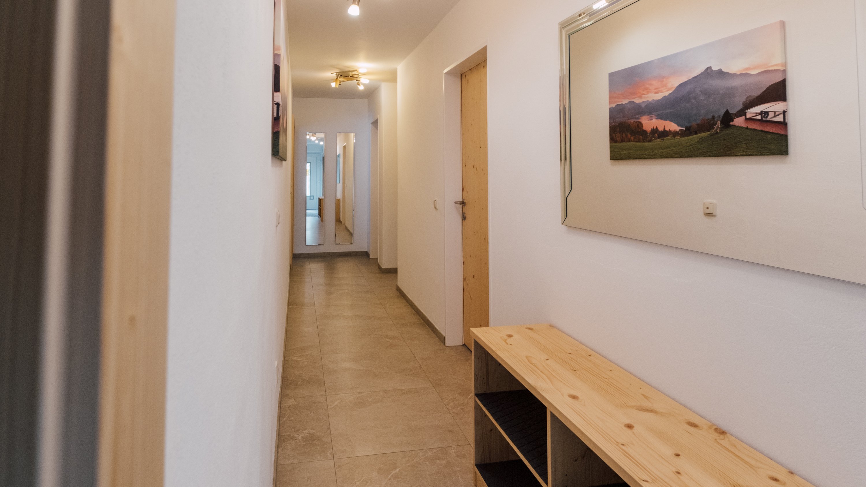 Heller Flur mit einer Holzbank und einem Spiegel an der Wand in minimalistischer Einrichtung