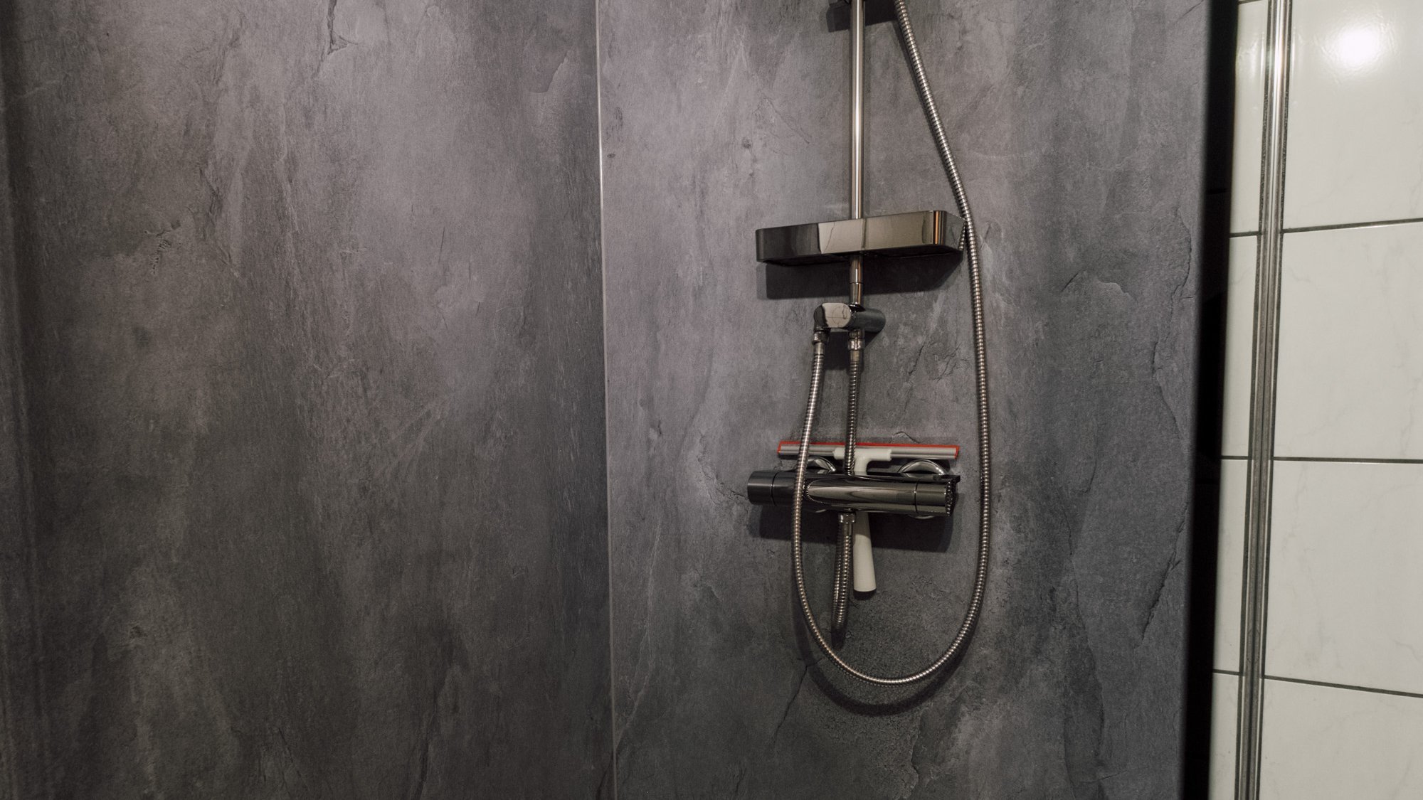 Moderne Dusche mit Regenbrause und Ablage für Toilettenartikel an einer strukturierten Wand