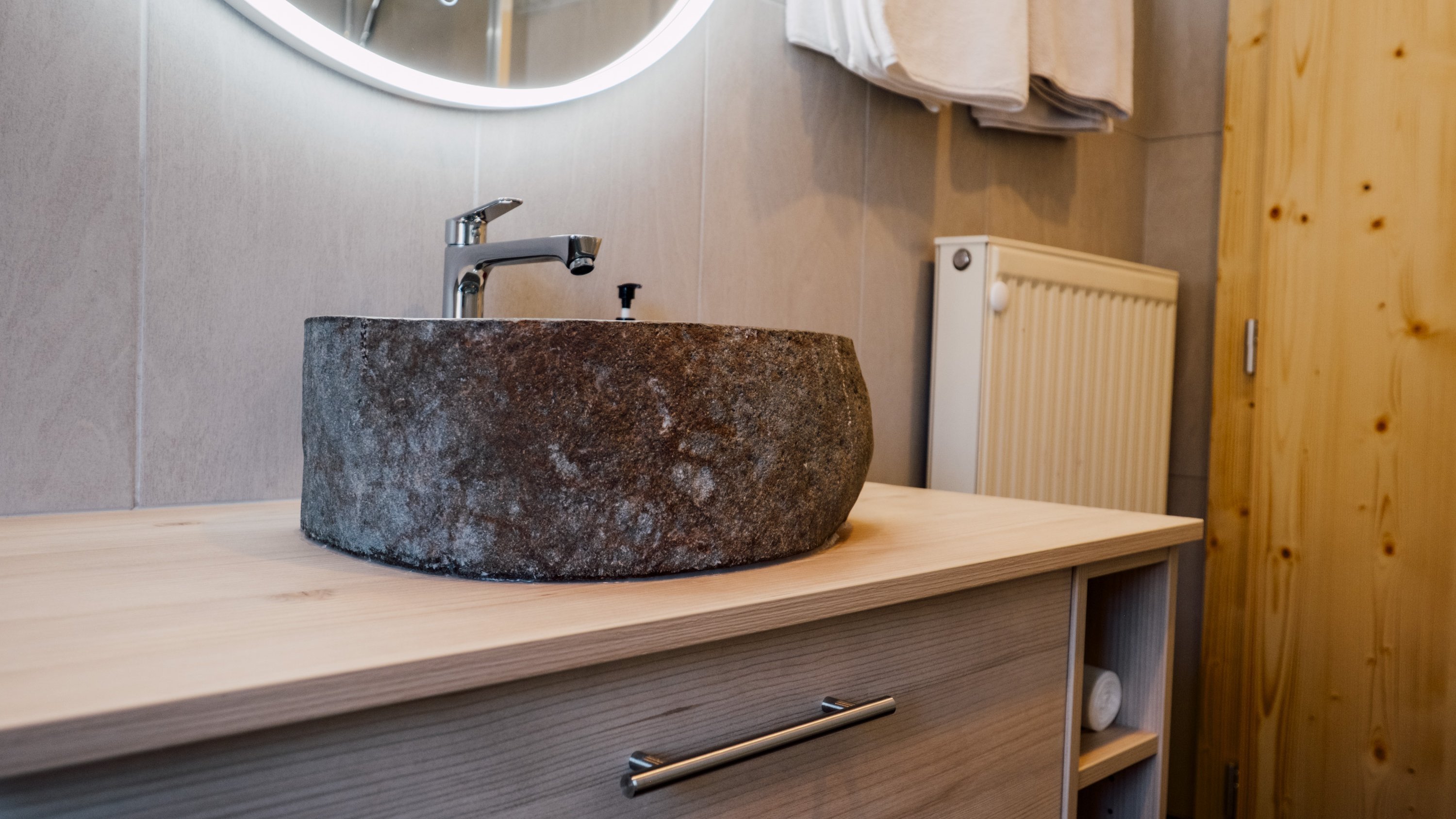 Badezimmer mit einem einzigartigen Steinwaschbecken auf einem Holzschrank und einem runden Spiegel