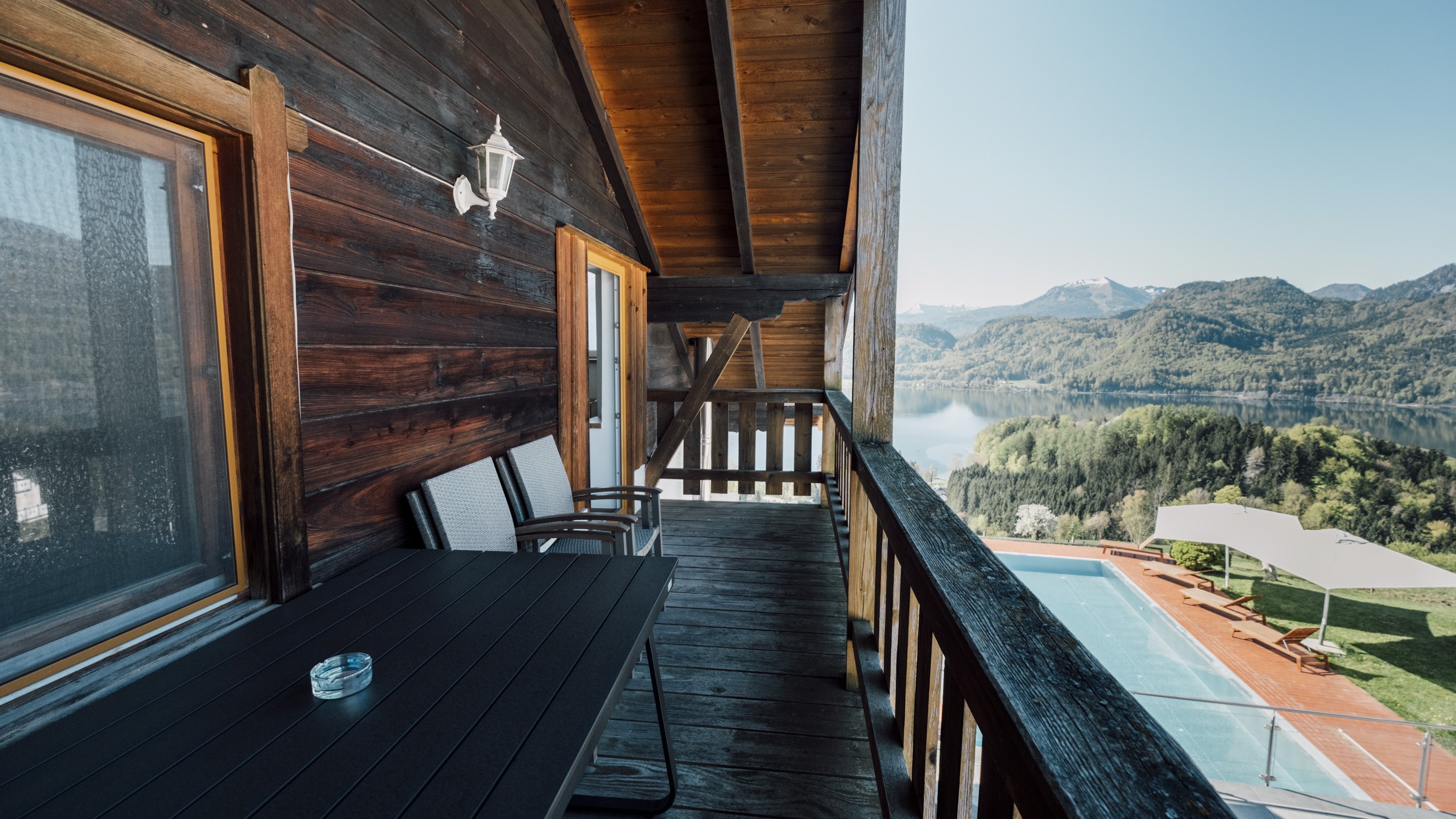 Holzbalkon mit Sitzgelegenheiten und Blick auf eine malerische Berglandschaft und einen Swimmingpool