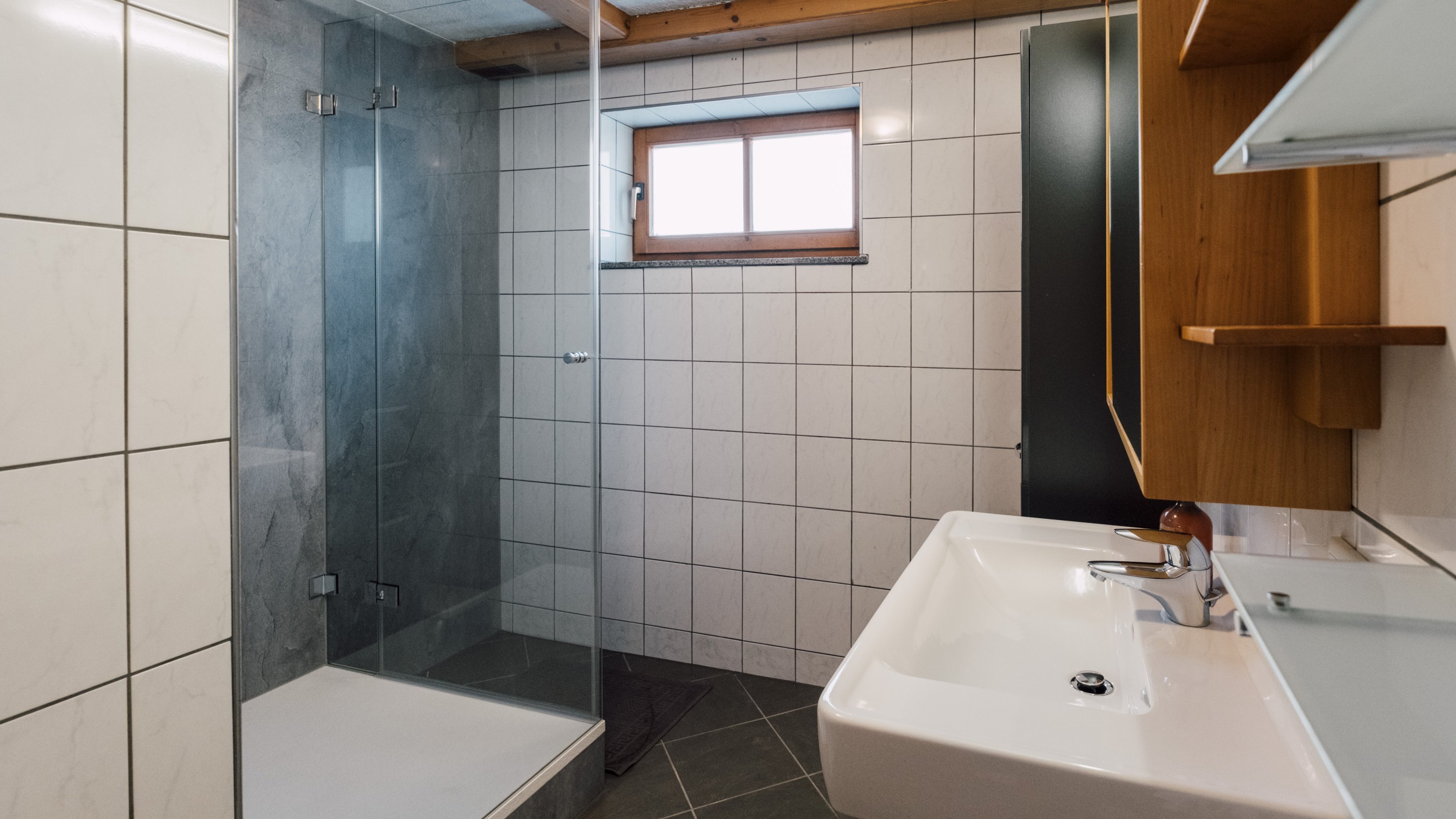 Badezimmer mit Glasdusche, Wandwaschbecken und gefliesten Wänden und Böden zu sehen
