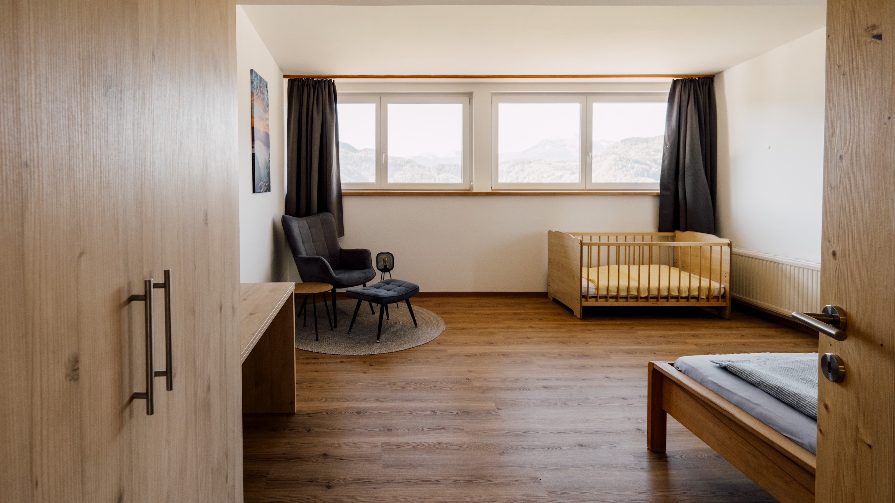 Helles, modernes Schlafzimmer mit einem Kinderbett und großen Fenstern für Tageslicht.