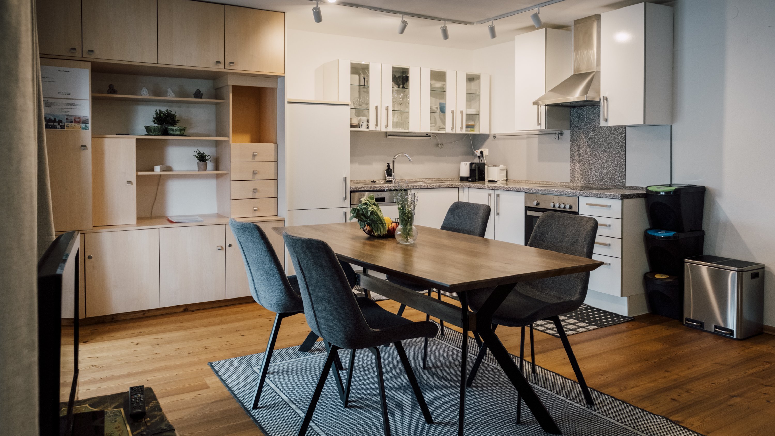 Eine moderne Küche mit einem Holztisch und Stühlen im Essbereich sowie Küchenschränken und Geräten
