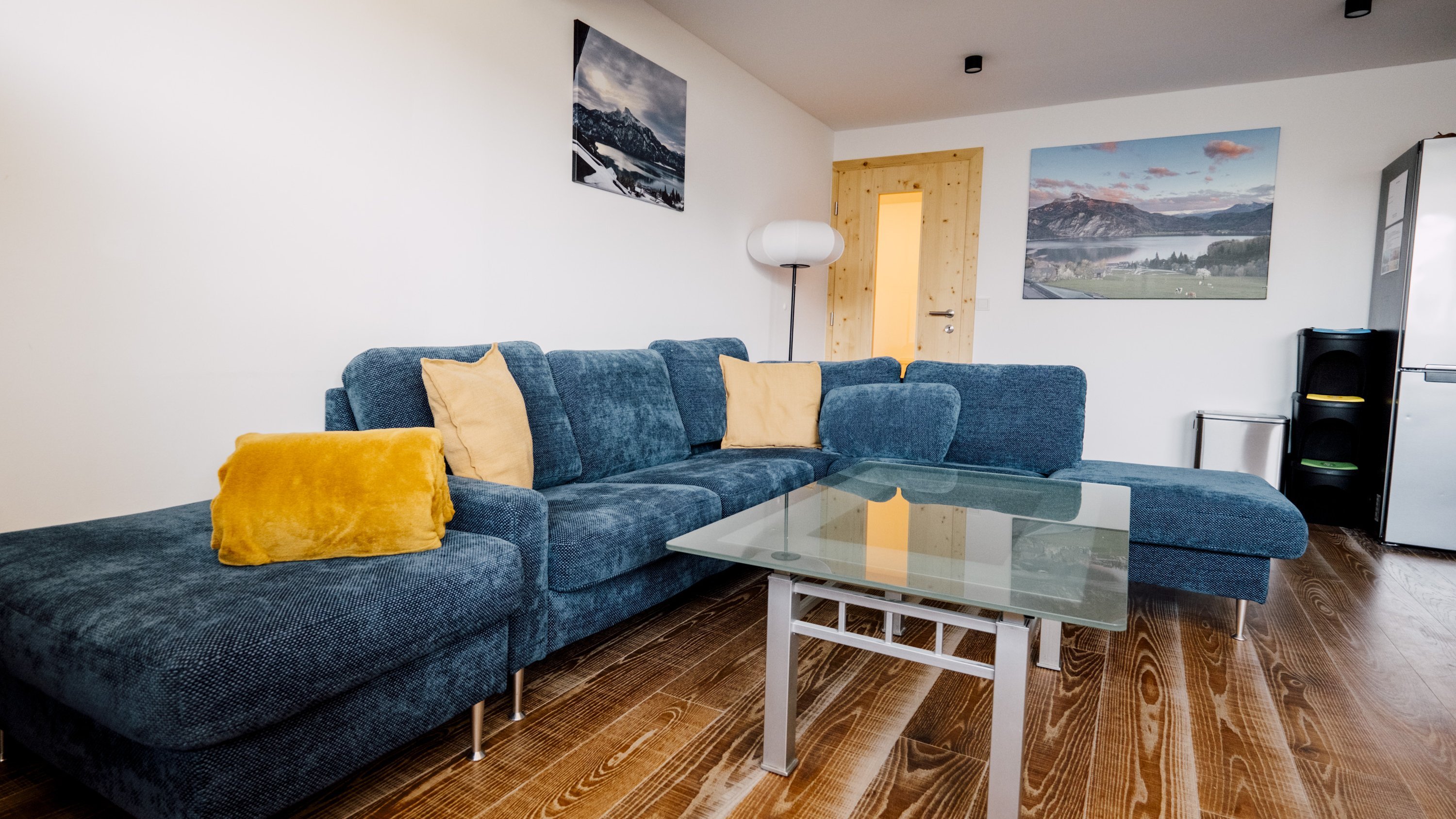 Modernes Wohnzimmer mit einem blauen Sofa, Glastisch und Holzboden für eine gemütliche Einrichtung