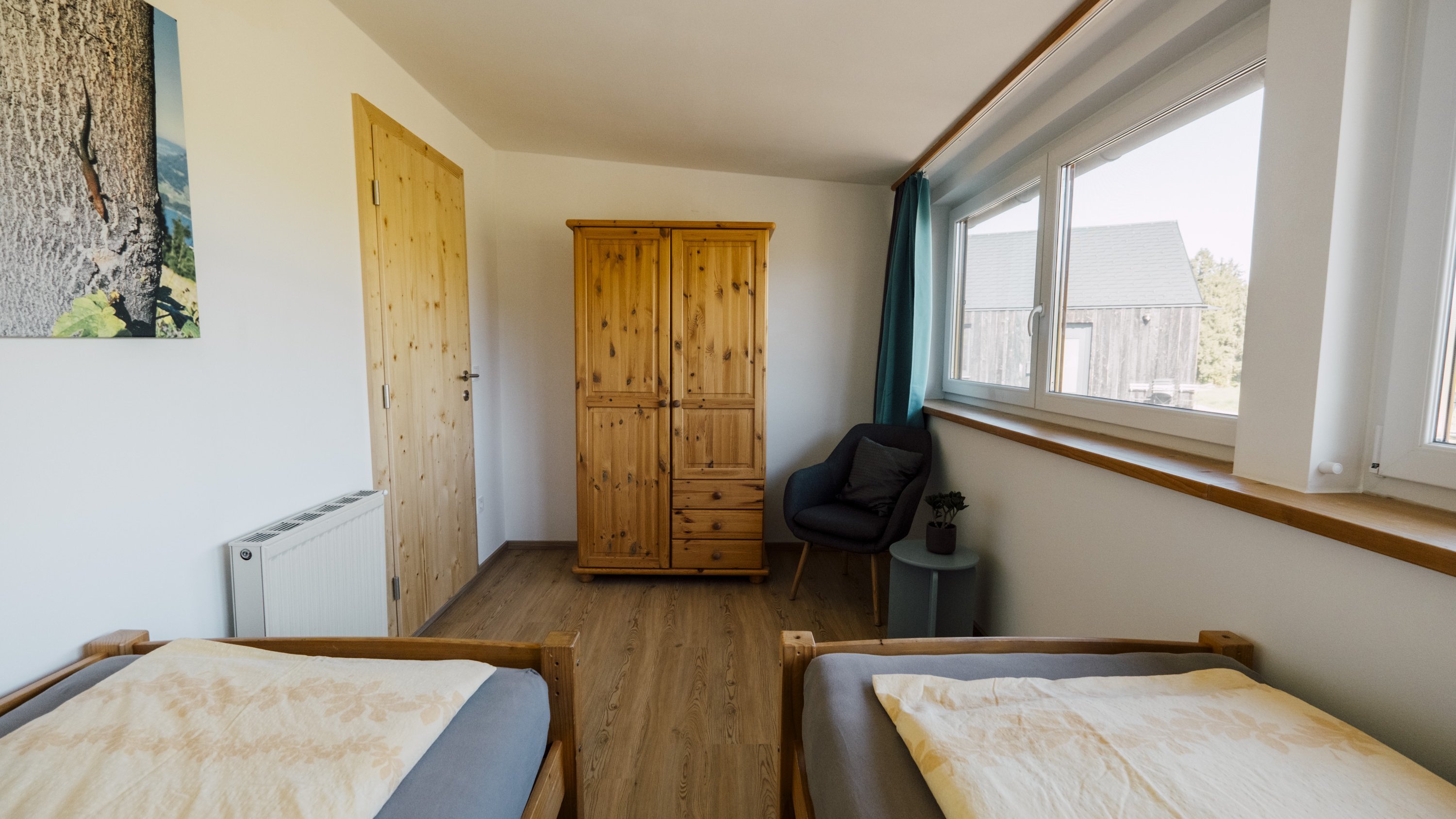 Ein gut beleuchtetes Schlafzimmer mit zwei Einzelbetten, einem Holzschrank und einem Stuhl