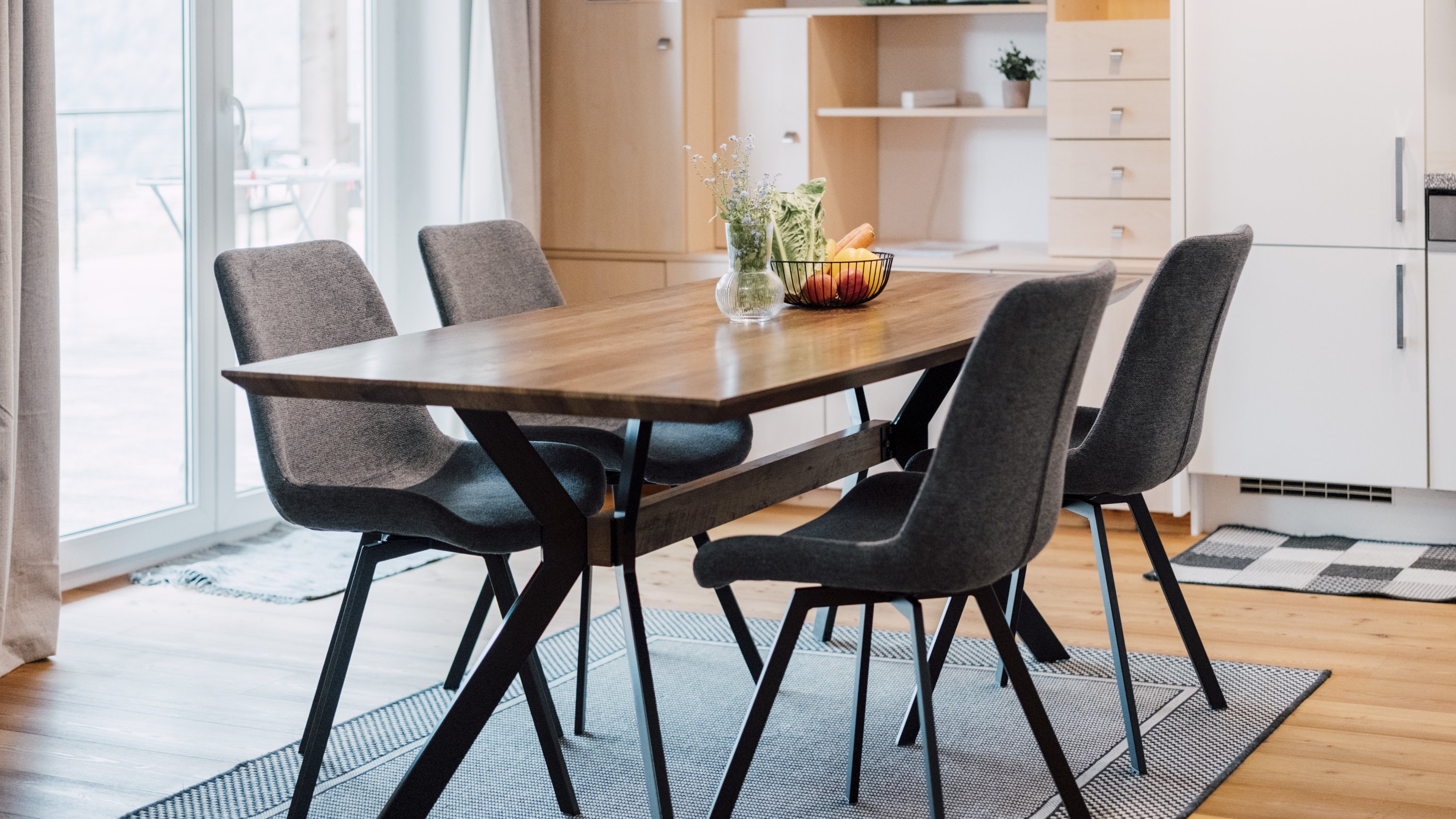 Esszimmer mit einem Holztisch und vier gepolsterten Stühlen auf einem gemusterten Teppich