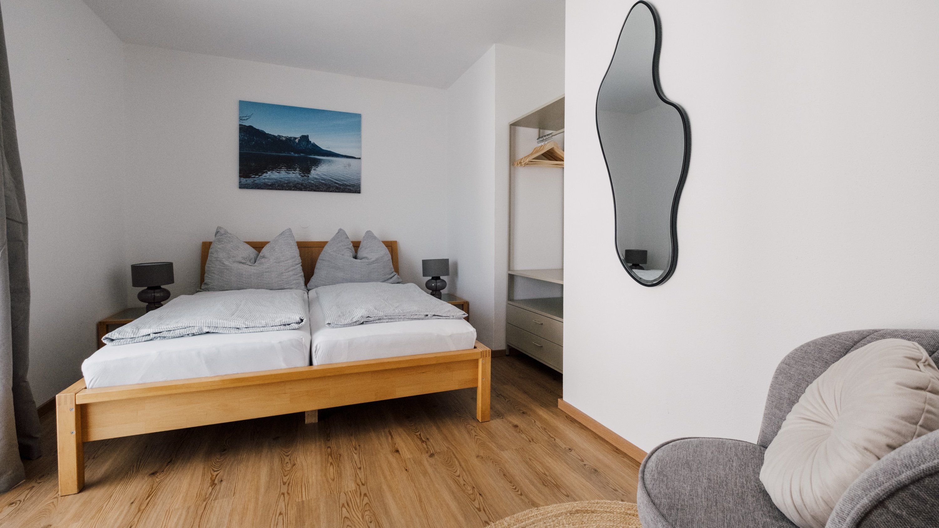 Modernes Schlafzimmer mit Holzdetails Schlafzimmer mit Holzbetten, grauer Bettwäsche und gemütlichem Stuhl in modernem Stil.