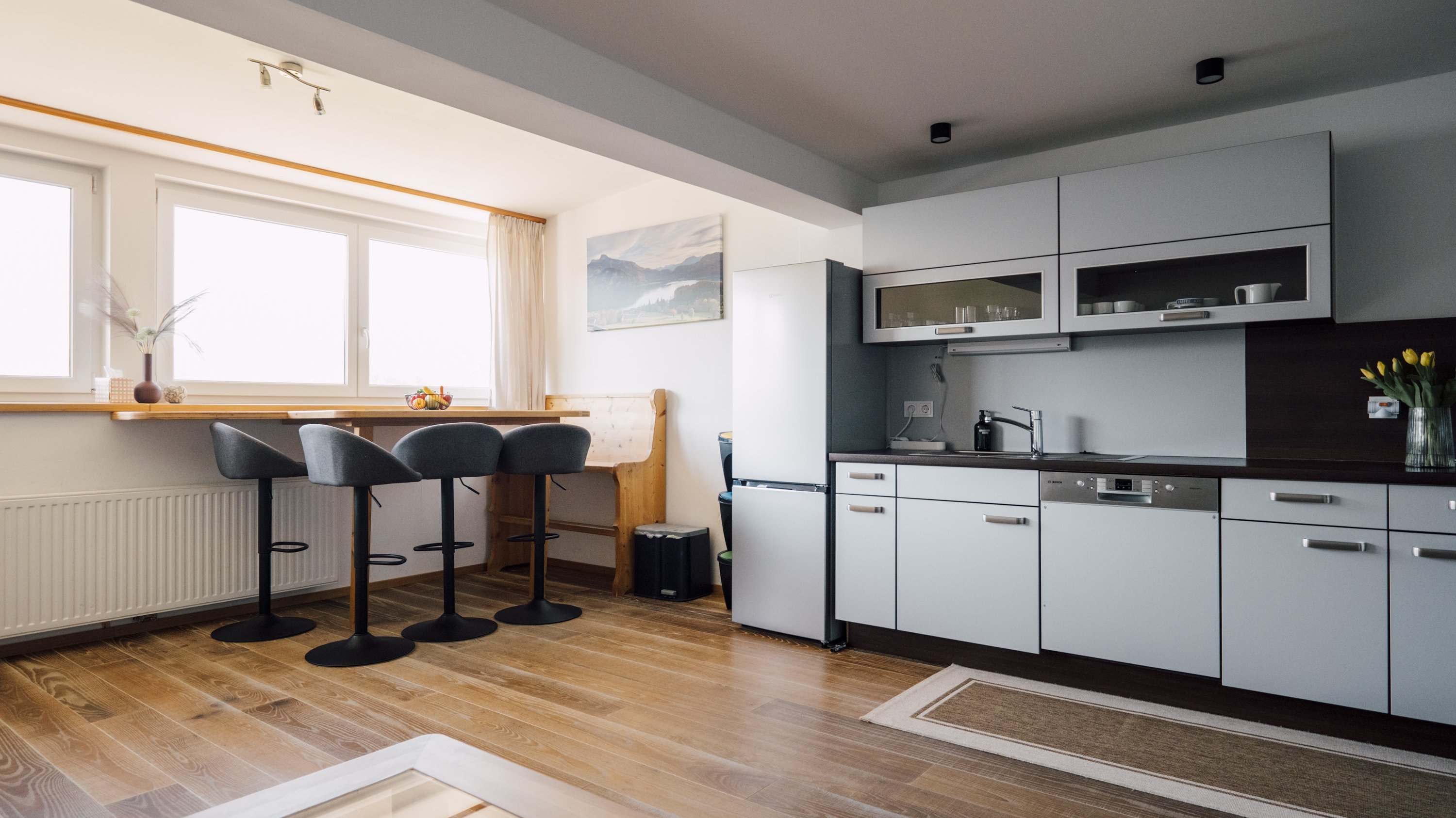 Helle, moderne Küche mit eleganten Möbeln und Essbereich mit Barhockern unter großen Fenstern