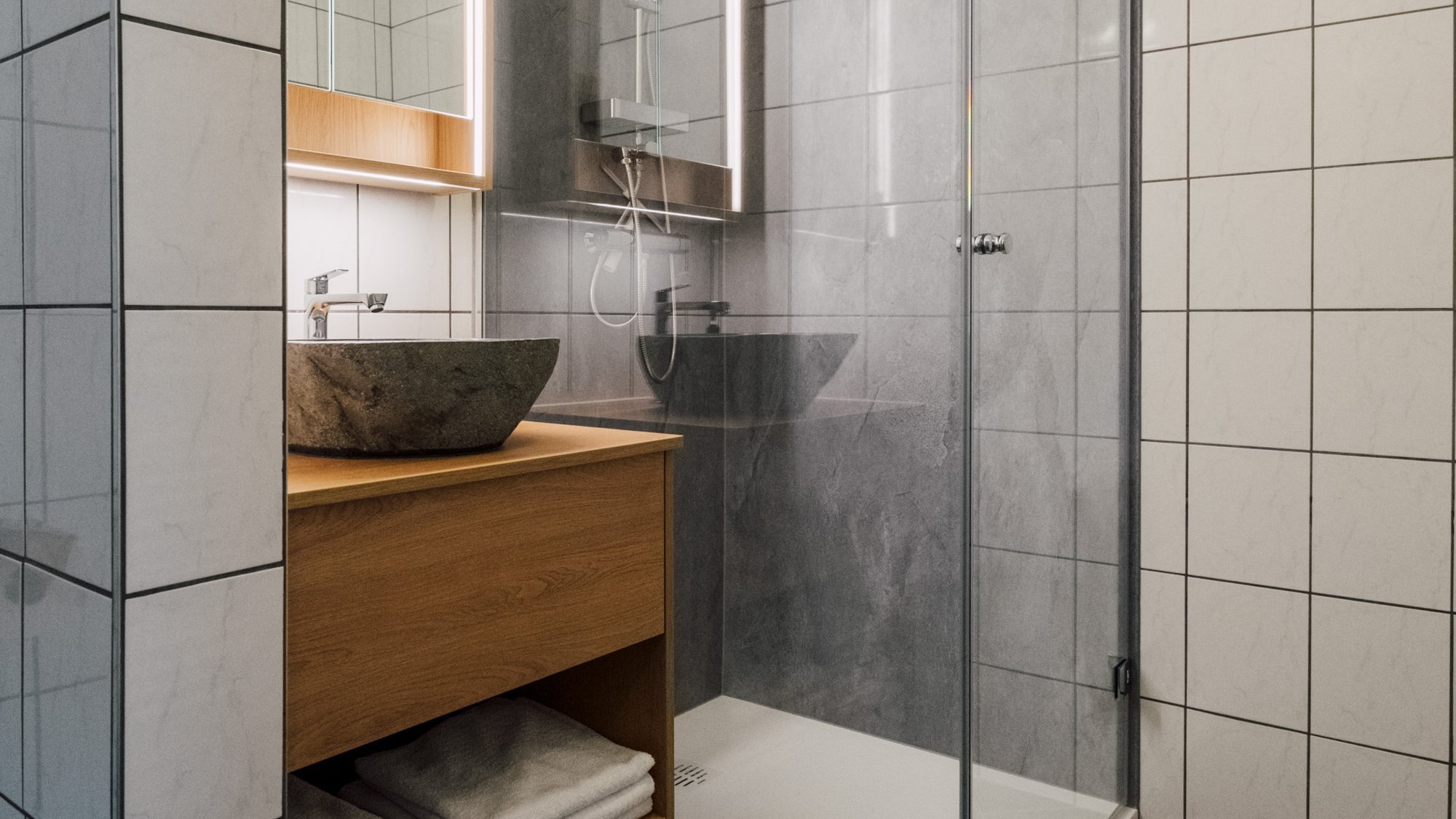 Modernes Badezimmer mit Glasdusche und Holzwaschtisch, gefalteten Handtüchern auf der Ablage.