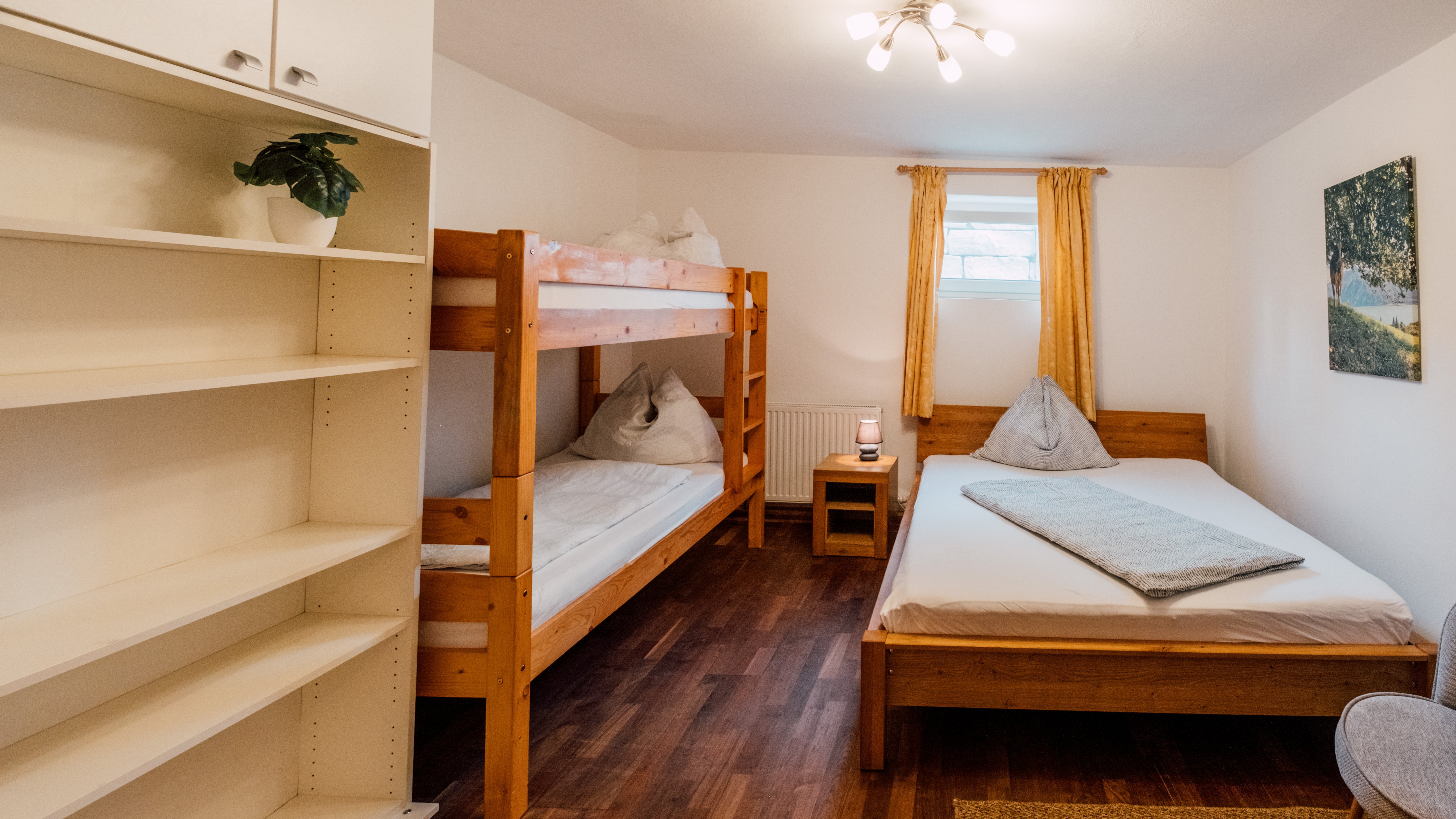 Ein gemütliches Schlafzimmer mit einem Etagenbett und einem Einzelbett aus Holz, warmen Farbtönen und moderner Einrichtung.