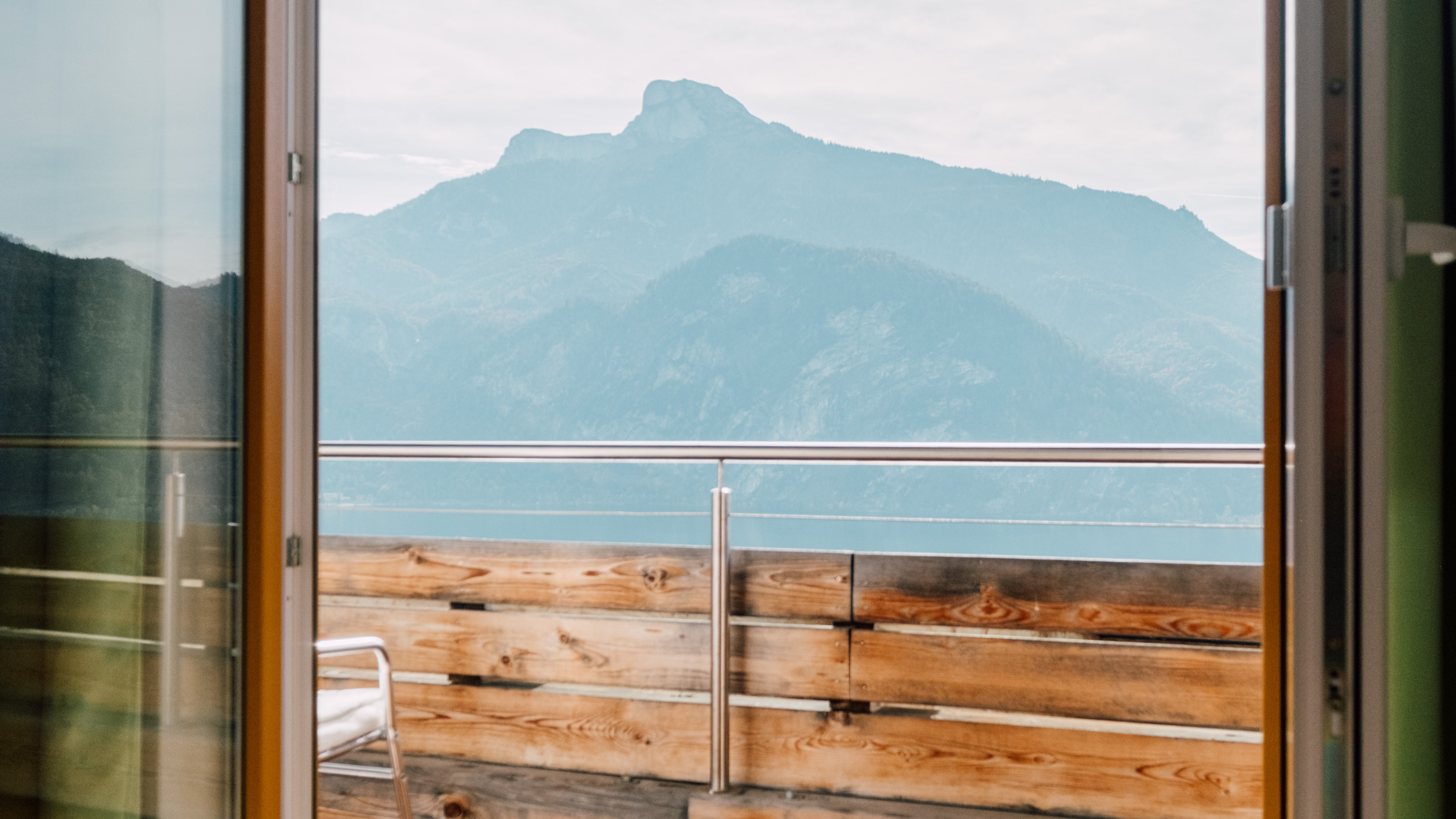 Interior view through glass doors showing balcony with wooden railing and mountain landscape