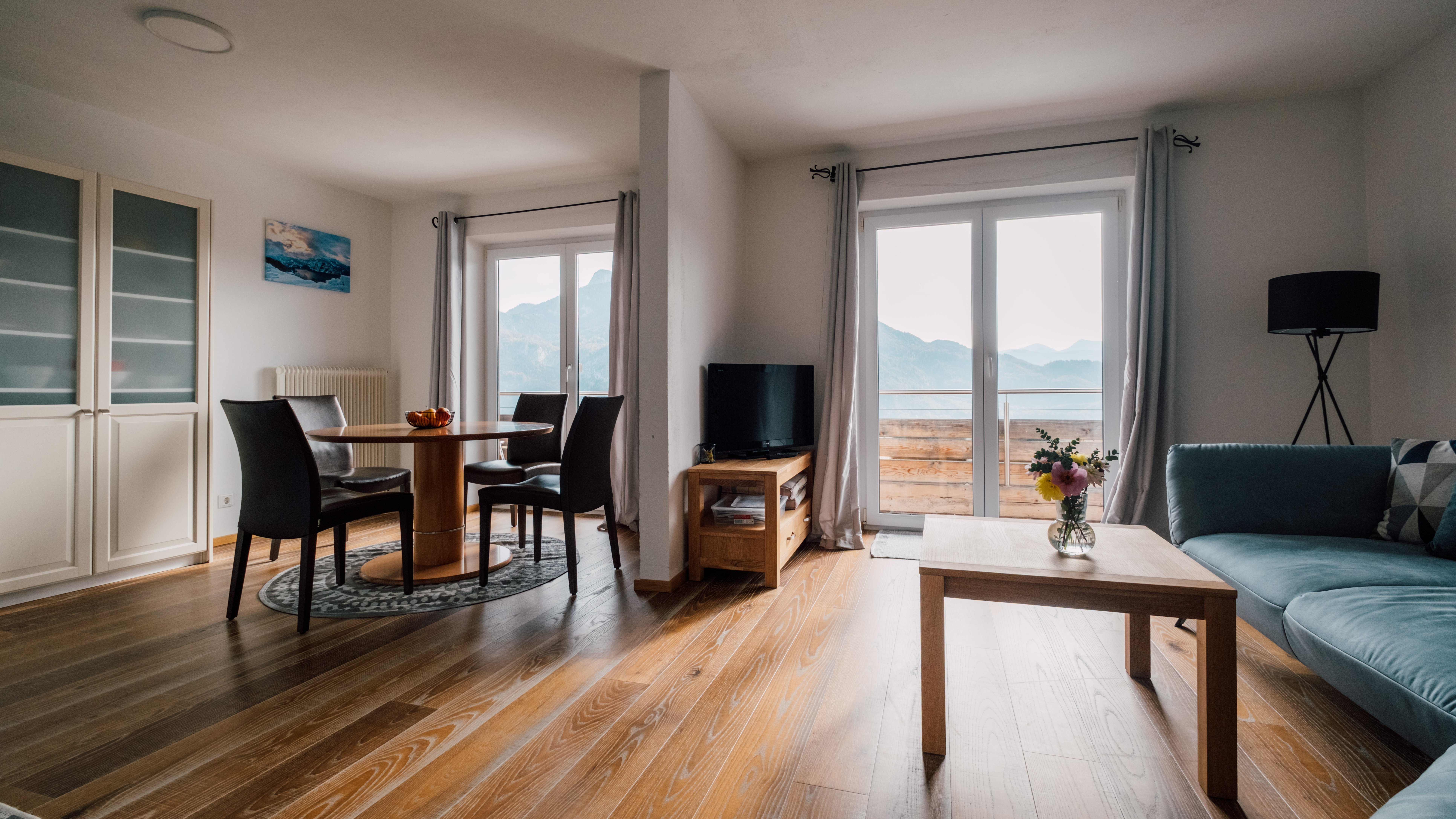 Ein modernes Wohnzimmer mit großen Fenstern und Blick auf Berge, ausgestattet mit Sofa und Tisch.