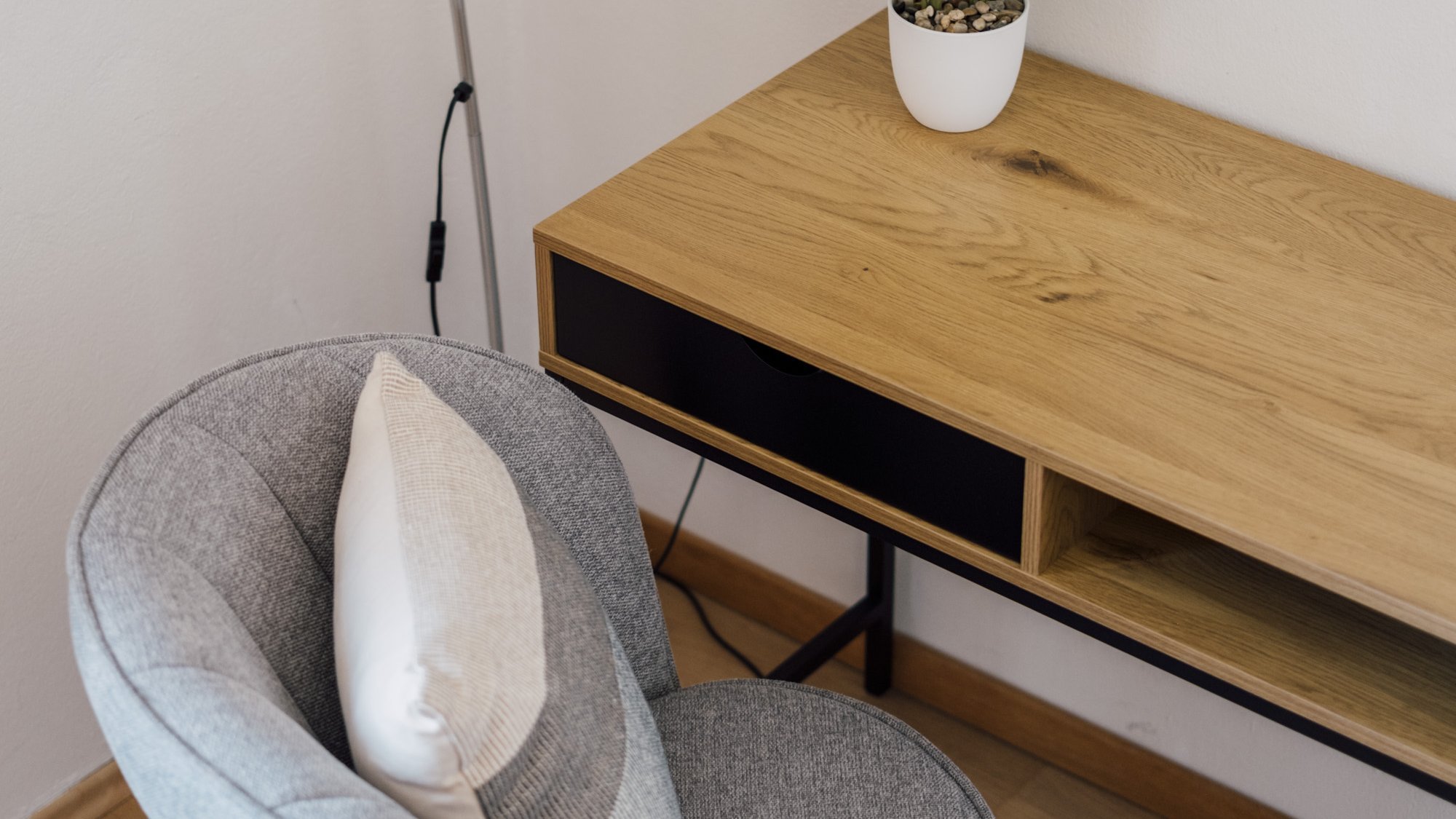 Helles Home Office mit Holzschreibtisch, grauem Stuhl und Pflanze auf dem Tisch.