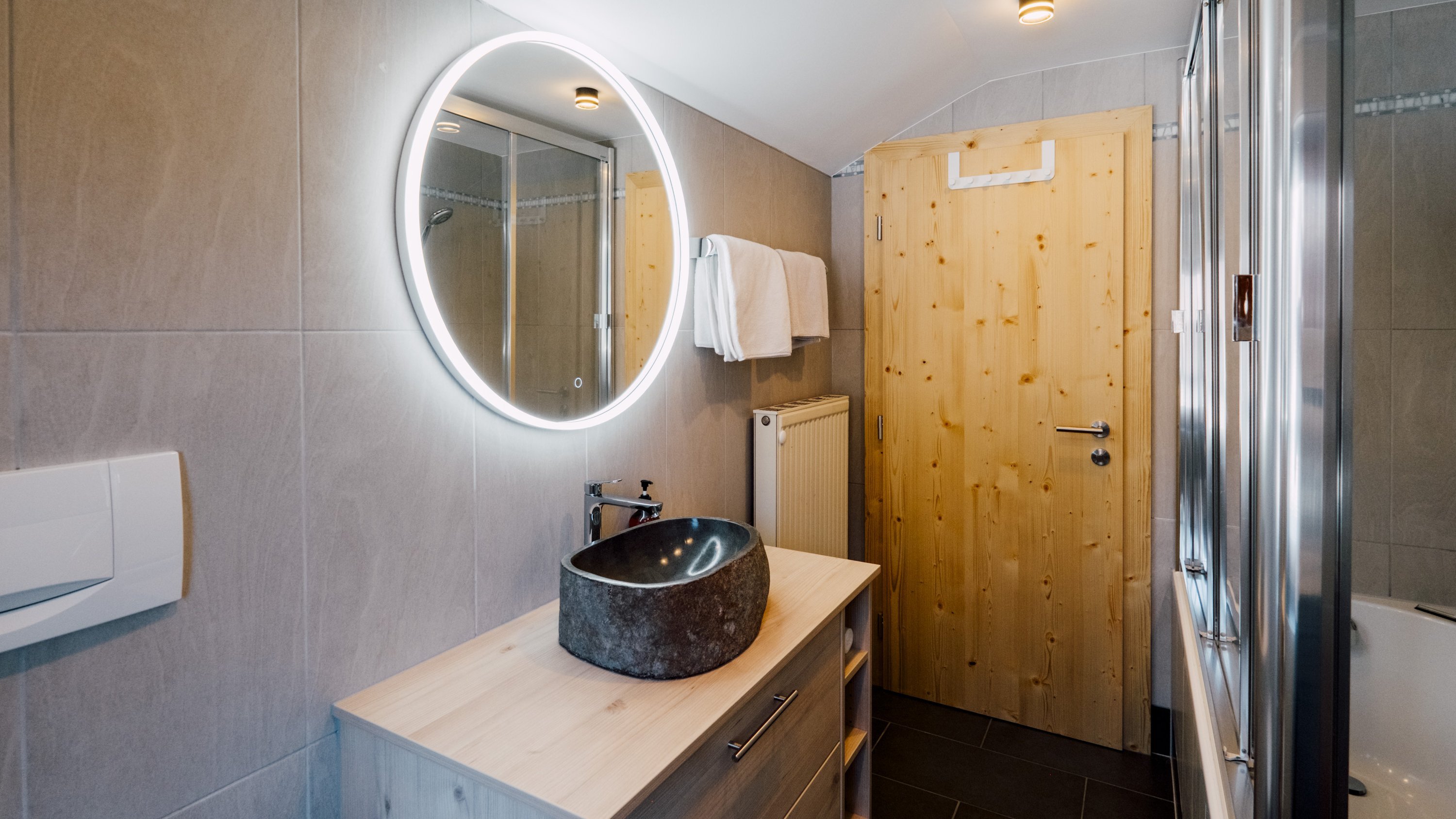 Badezimmer mit runder Spiegel, Steingewässer und Holzwaschtisch an einer Holztür