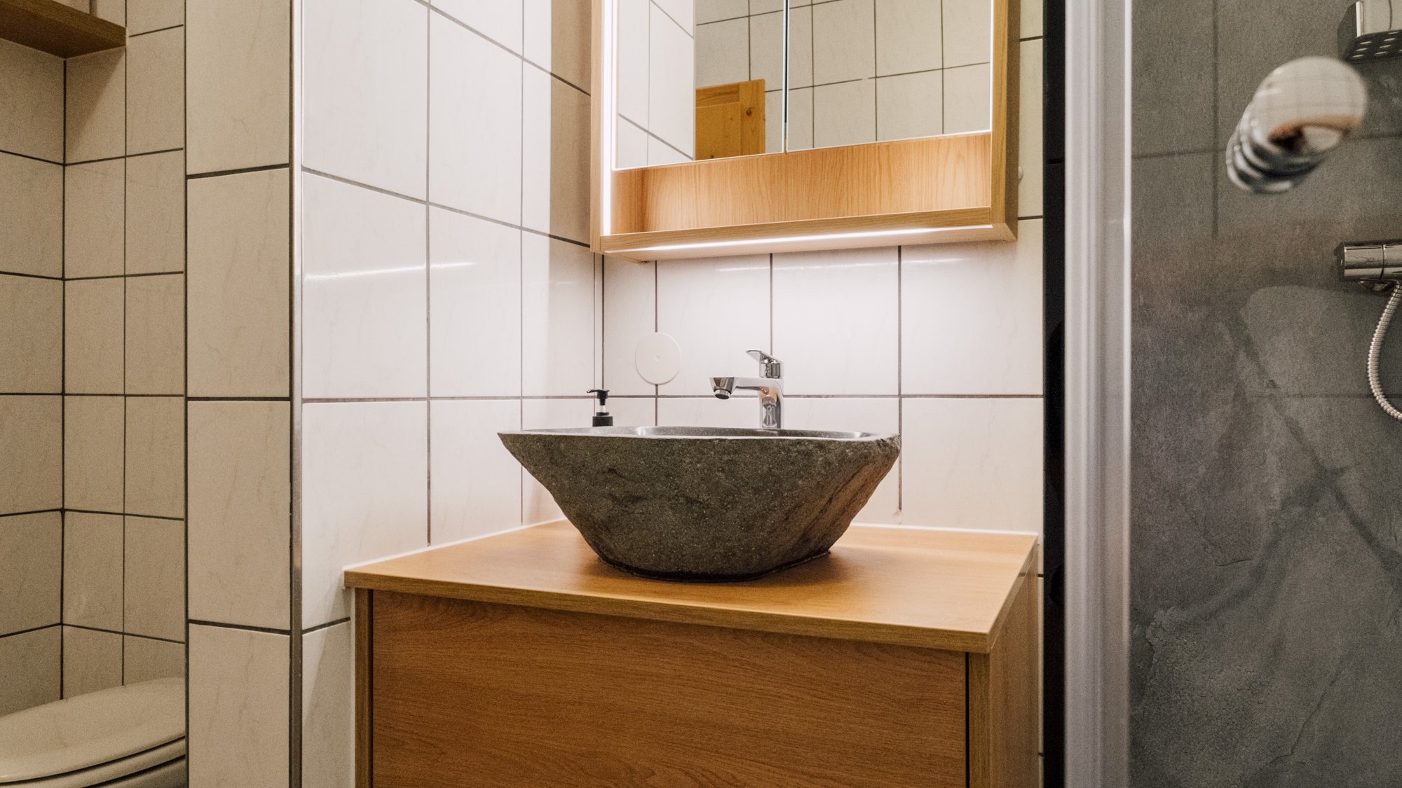 Ein modernes Badezimmer mit einem eleganten Waschbecken und Holzunterschrank, dazu ein beleuchteter Spiegel und ordentlich dr