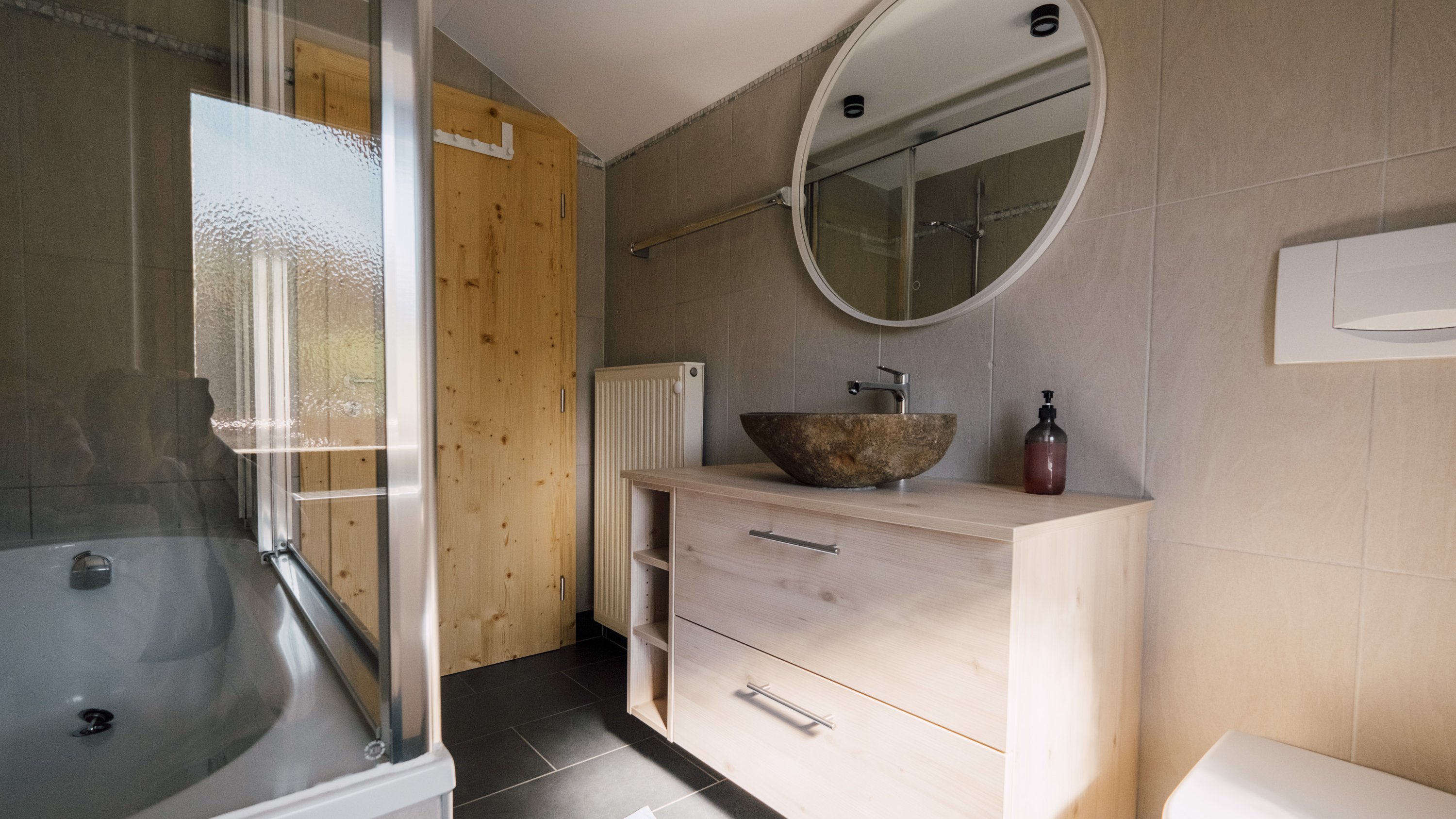 Badezimmer mit runder Spiegelfläche, Dusche und Badewanne in modernem Design ist sichtbar