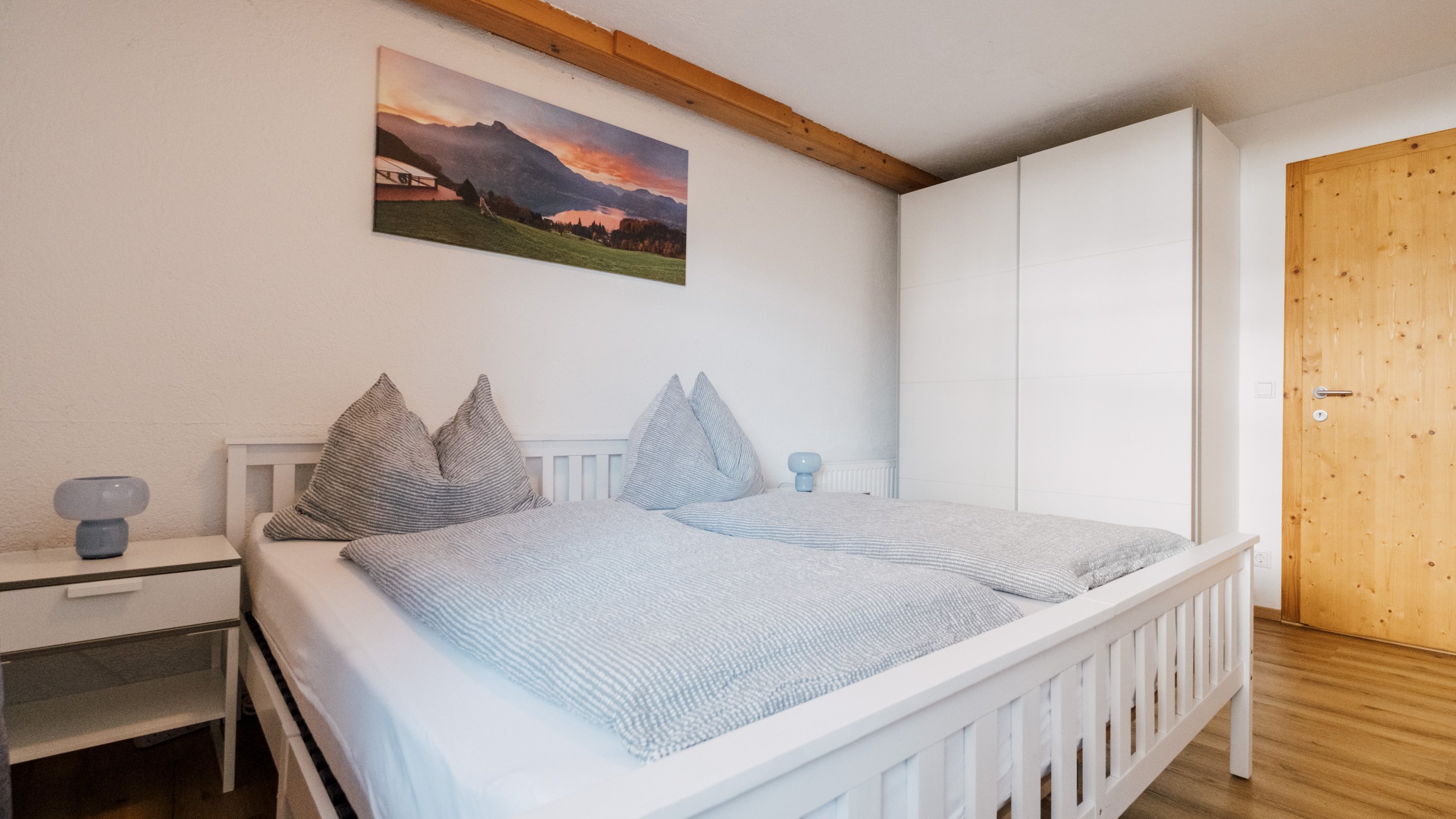 Gemütliches Schlafzimmer mit Doppelbett, Nachttisch und Berglandschaft auf der Wand