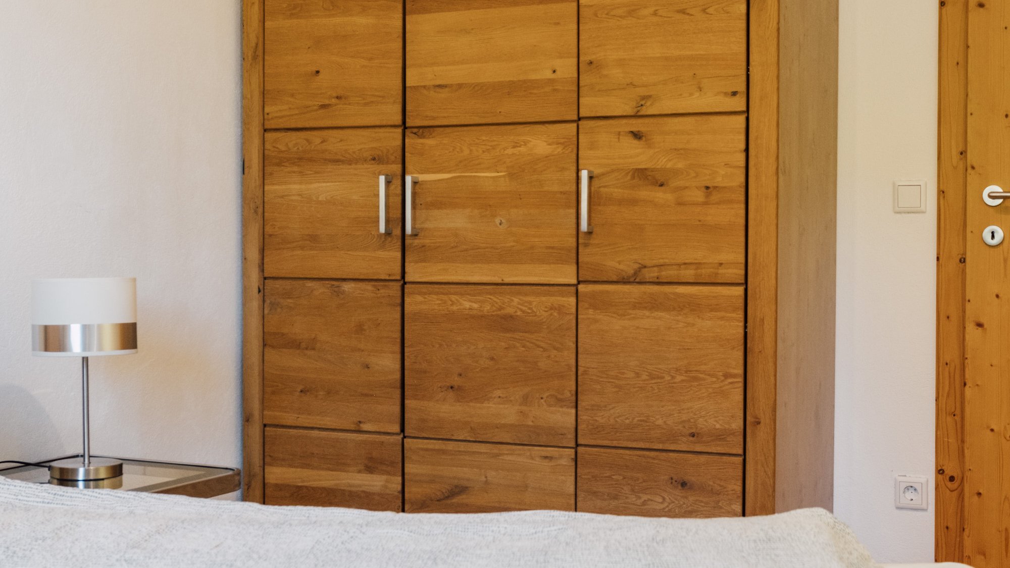 Helles Schlafzimmer mit einem Holzschrank und einem ordentlich bezogenen Bett mit einer hellen Decke.