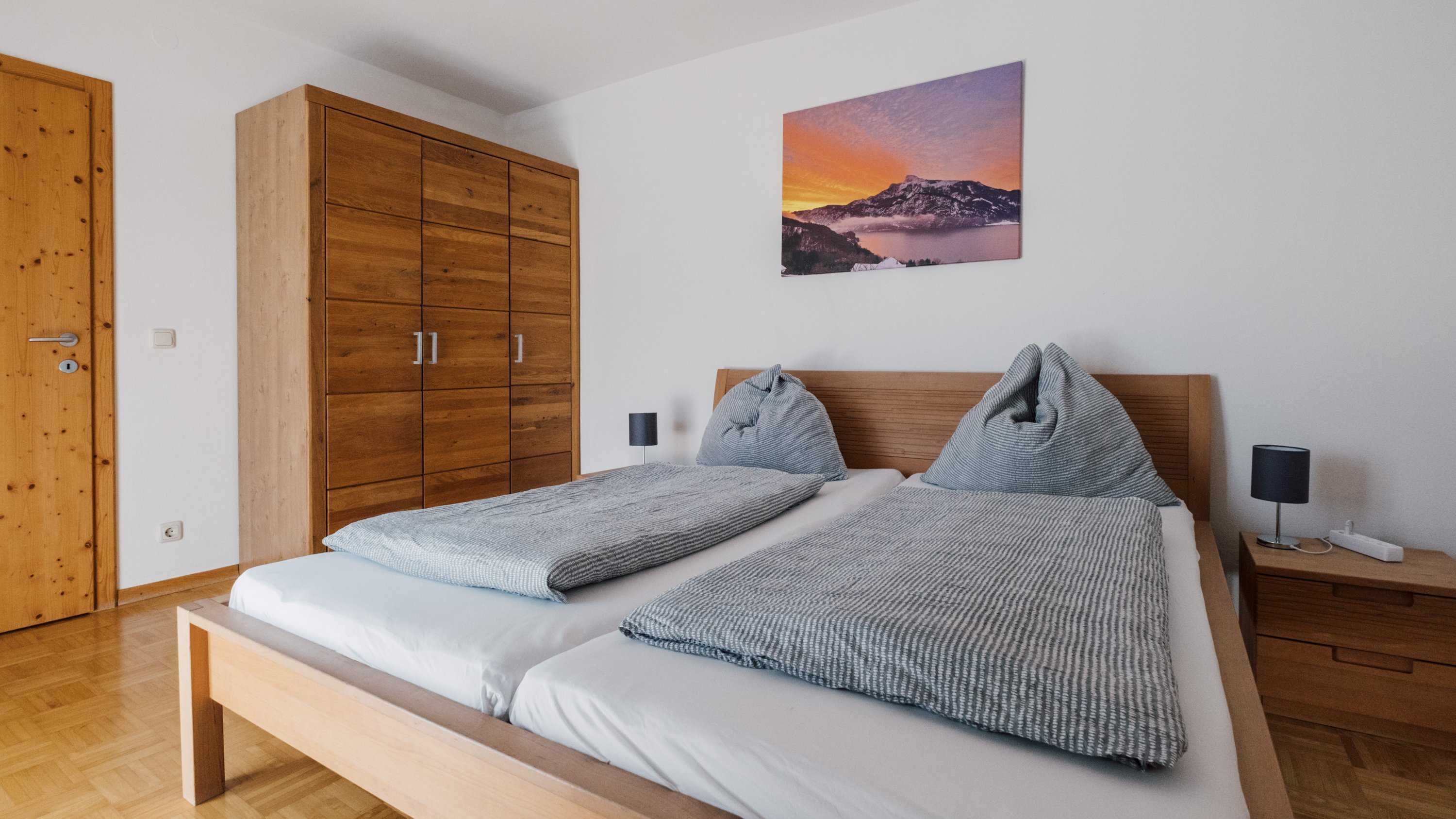Helles Schlafzimmer mit einem Holzbett, zwei Kissen und einem Schrank an der Wand