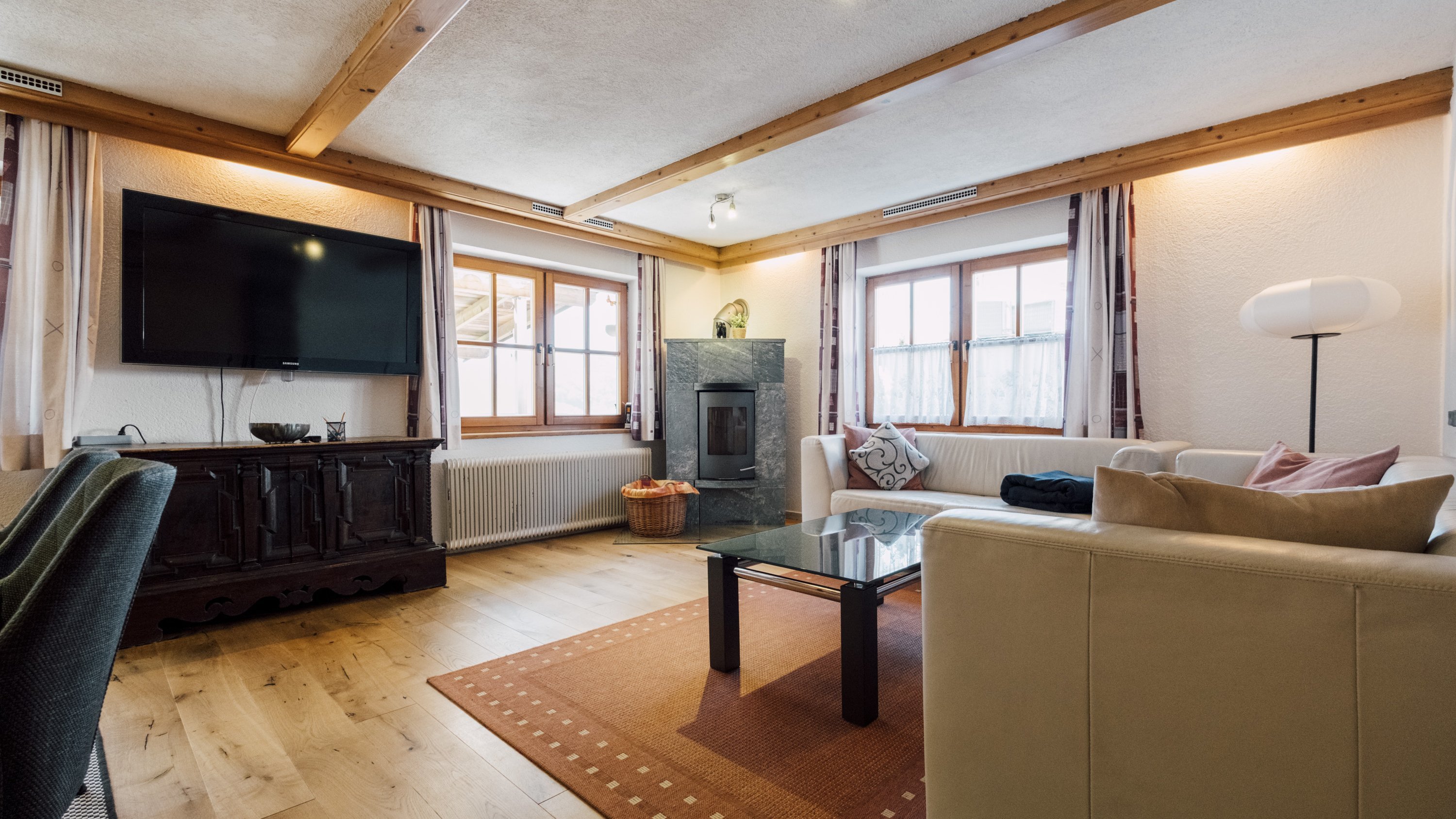 Gemütlicher Wohnraum mit Fernseher, Glastisch und bequemen Sitzgelegenheiten in einem modernen Design.