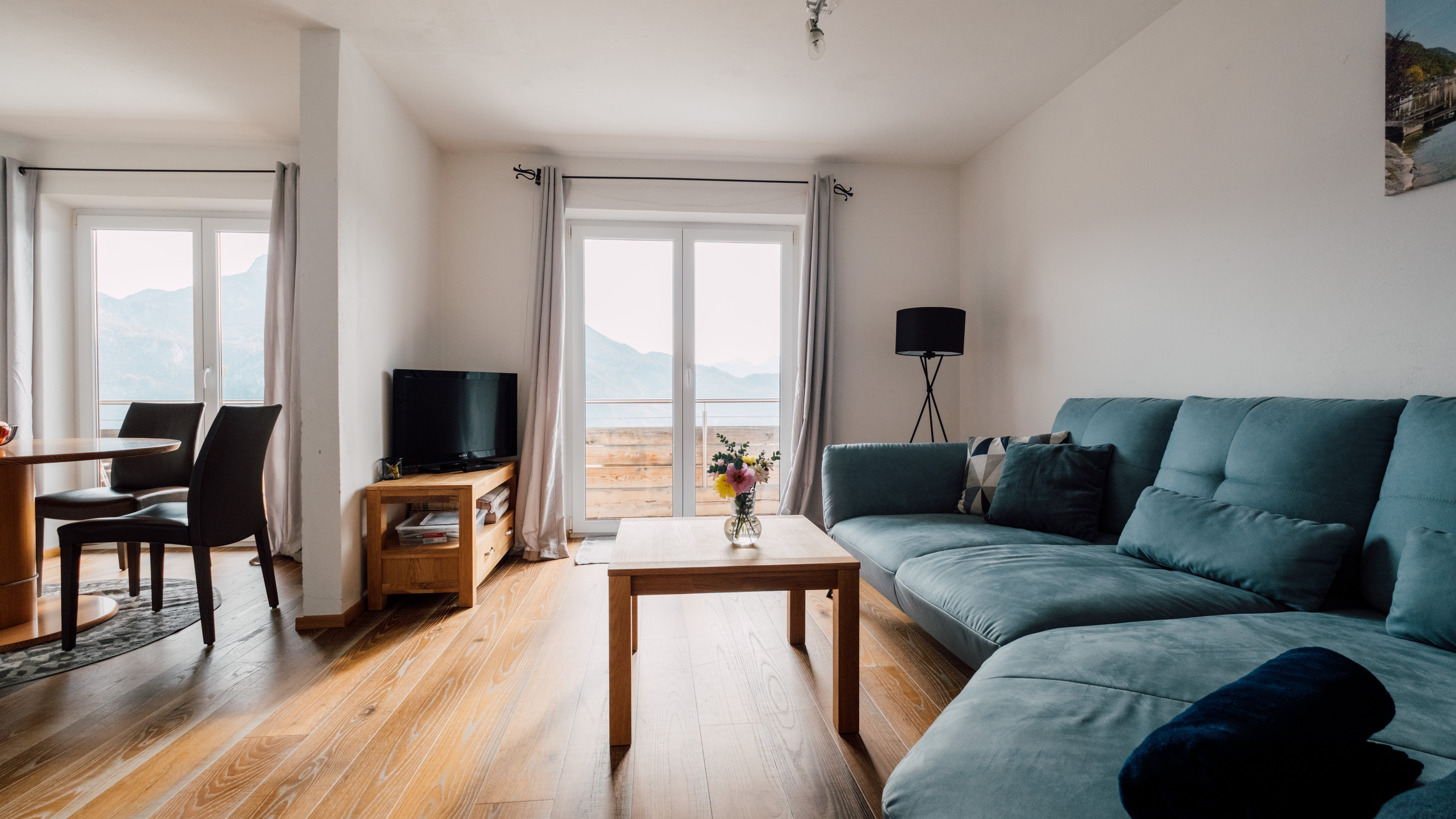 Gemütlicher Wohnraum mit Bergblick Moderner Wohnraum mit blauem Sofa, Holztisch und großen Fenstern zur Berglandschaft