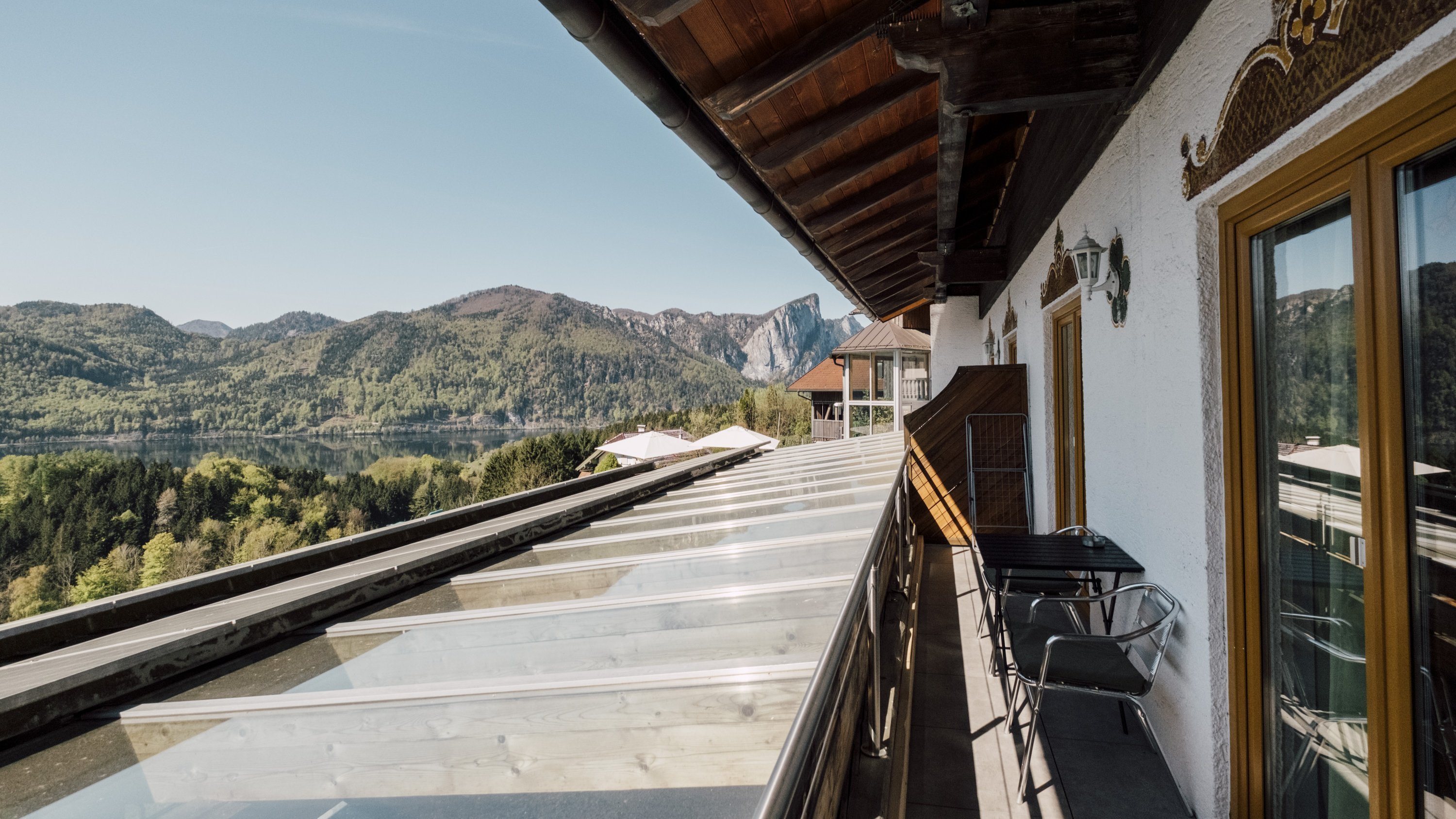 Balkon mit Glasgeländer und Ausblick auf Berglandschaft und Wasserfläche, Outdoor-Sitzgelegenheiten vorhanden