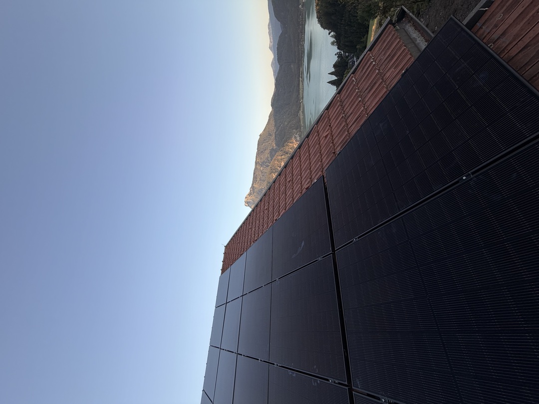 Photovoltaik-Module auf einem roten Ziegeldach, im Hintergrund der Mondsee und die Berge des Salzkammerguts