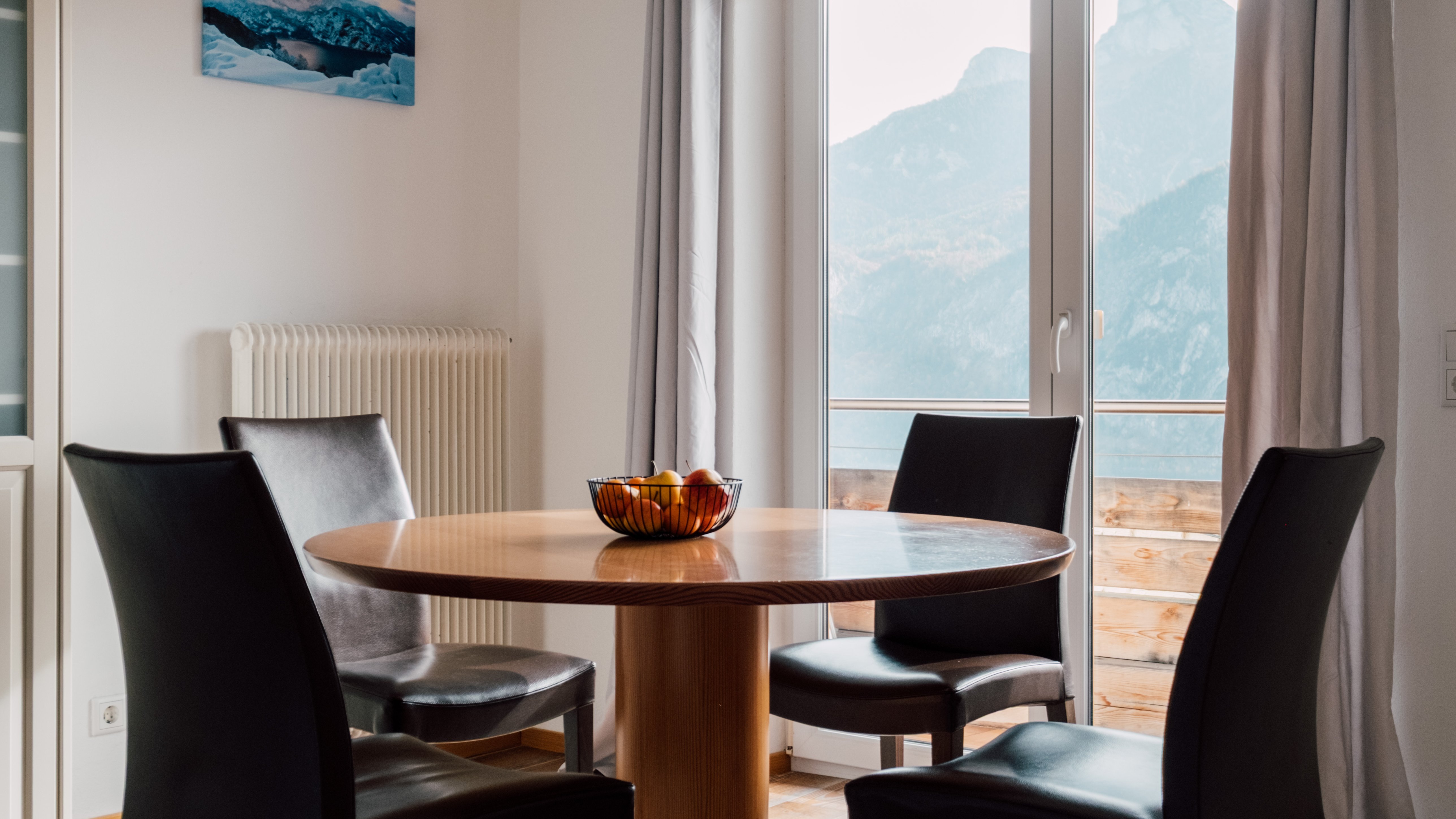 Moderner Essbereich mit Bergblick Heller Essbereich mit rundem Holztisch und vier schwarzen Stühlen vor großen Fenstern mit Aussicht auf Berge