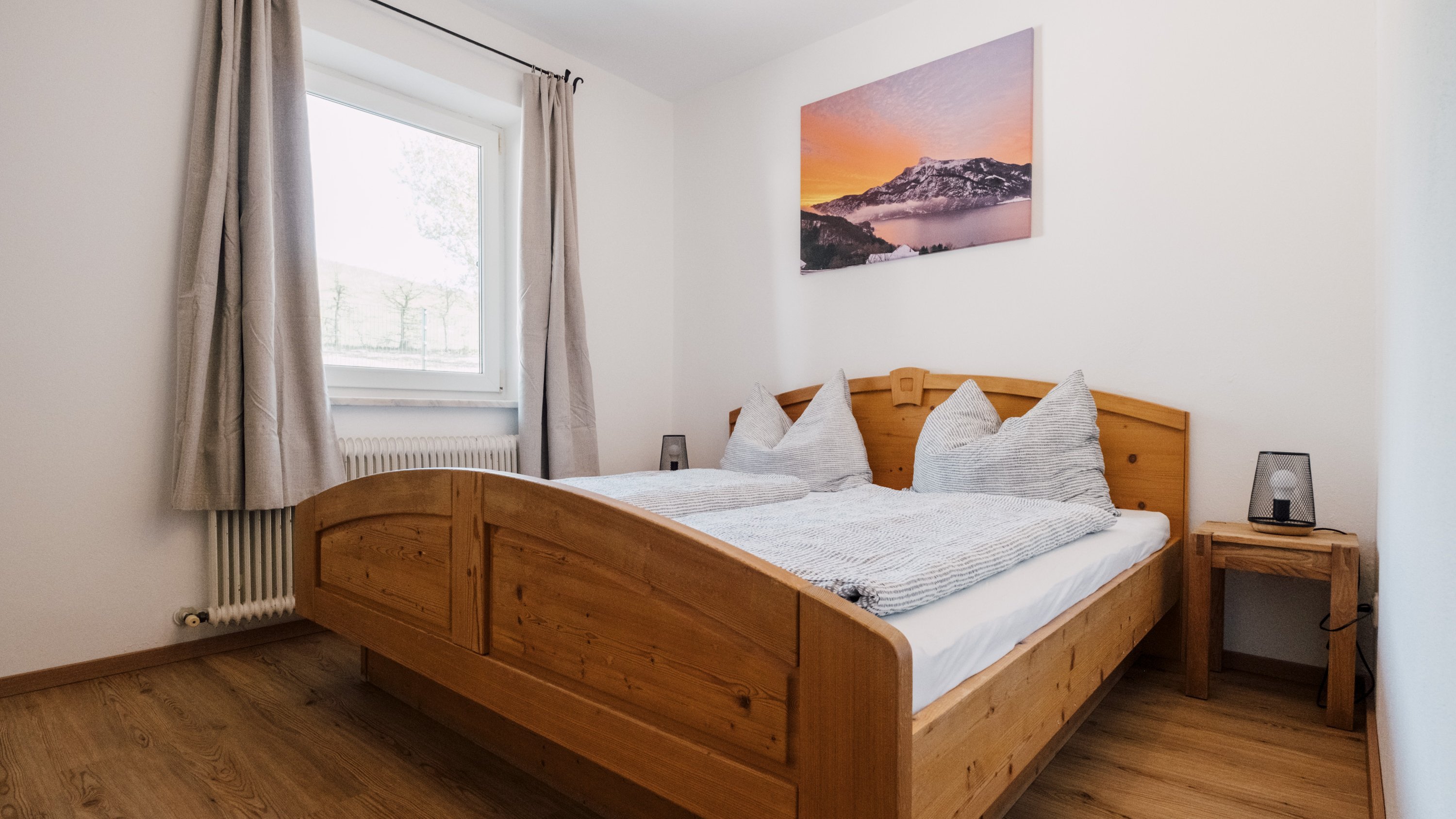 Gemütliches Schlafzimmer mit Holzmöbeln Ein einladendes Schlafzimmer mit einem Holzbett, grauen Kissen und einem Fenster für Tageslicht.