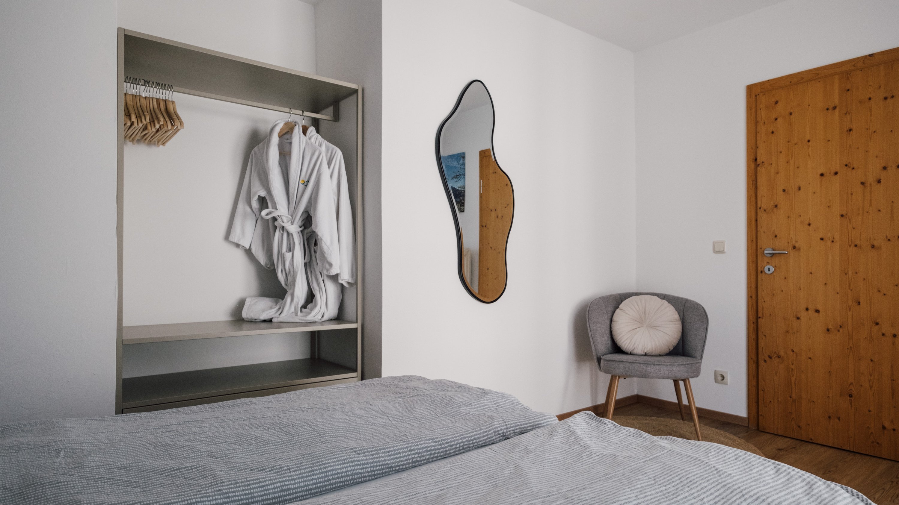 Minimalistisches Schlafzimmer im Mondseeblick Helles Schlafzimmer mit zwei Betten, Spiegel und einem offenen Kleiderschrank mit Bademantel.
