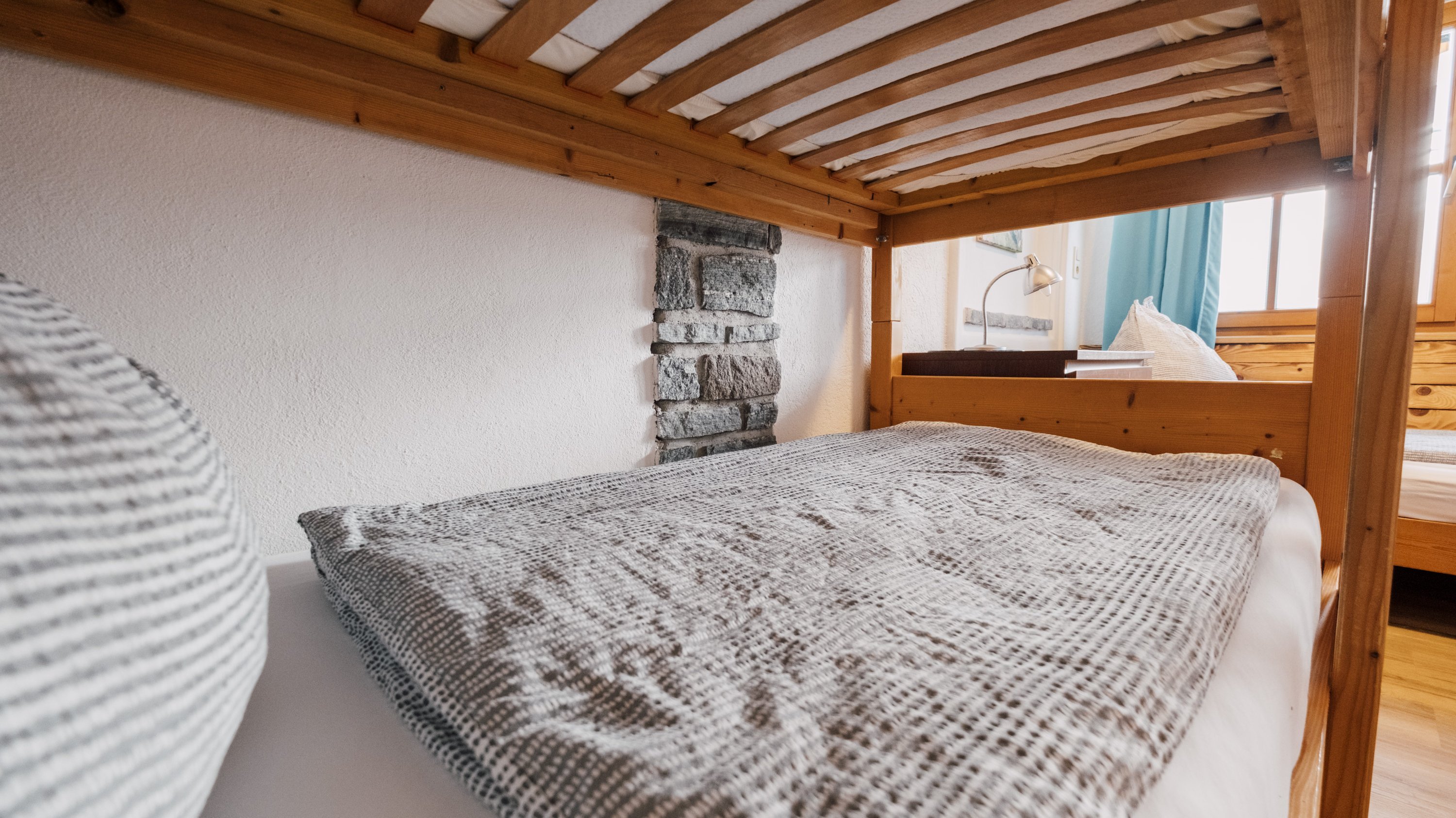 Nahaufnahme eines Etagenbetts in einem gemütlichen Schlafzimmer mit Holzrahmen und einer strukturierten Decke.