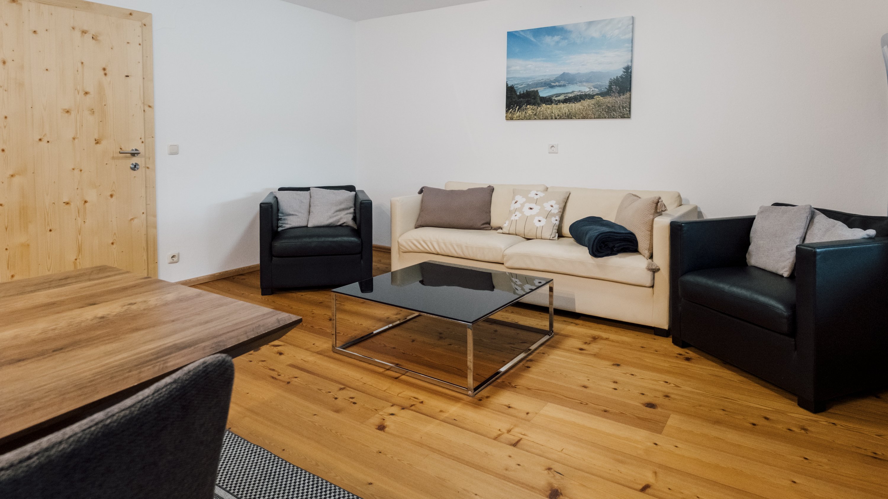 Gemütliches Wohnzimmer mit beigem Sofa, schwarzen Sessel und Glastisch auf Holzfußboden