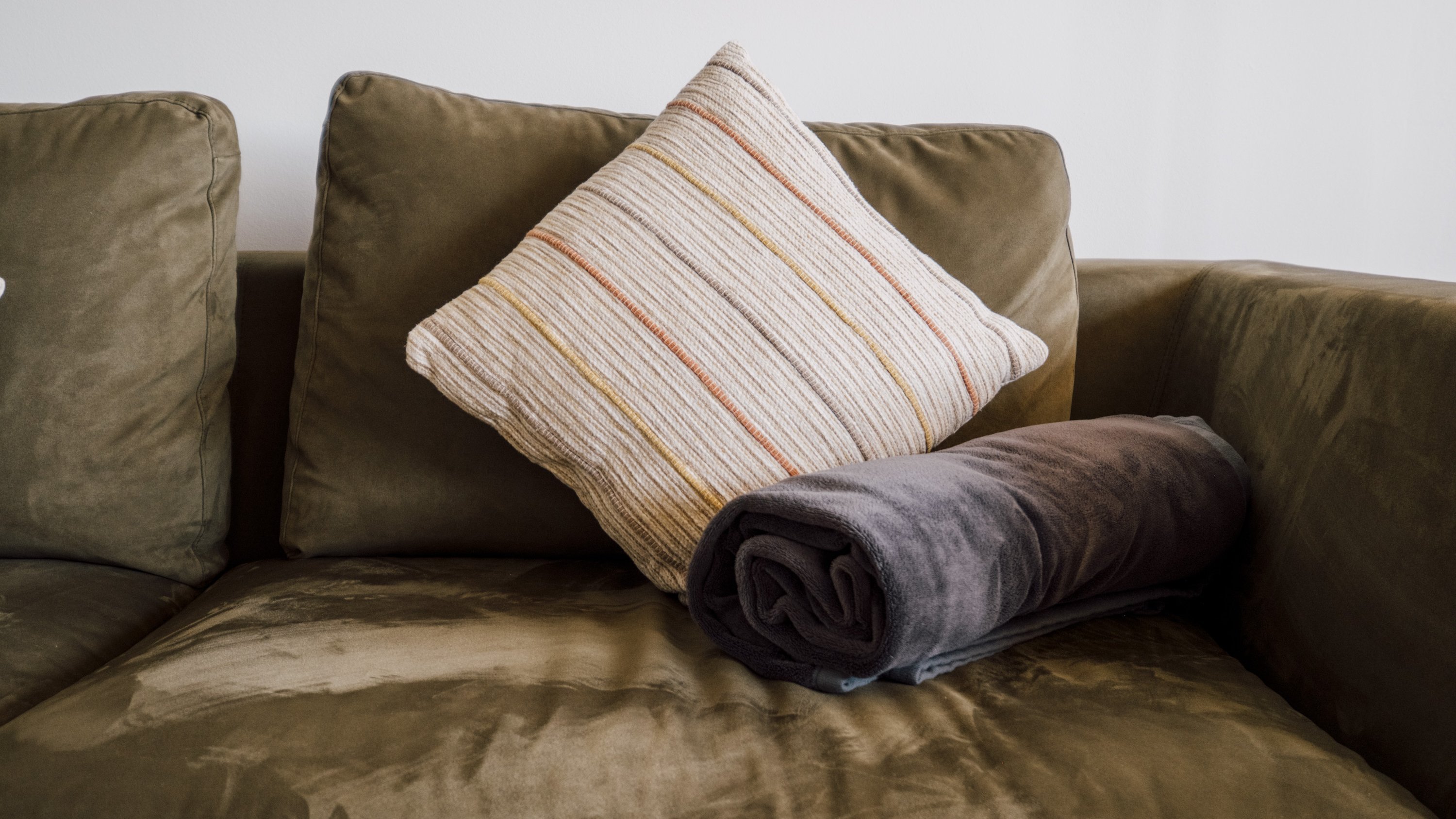 Sofa mit dekorativem Kissen und einer gerollten Decke darauf im Wohnzimmerbereich.